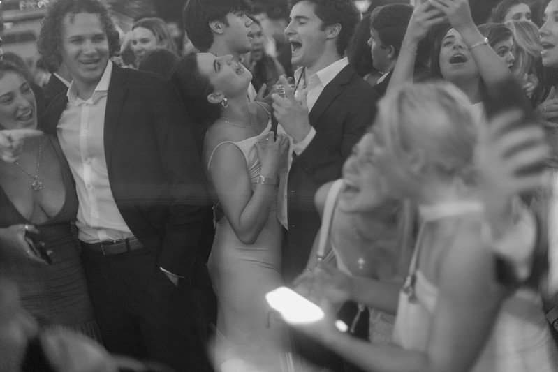 Group of people at a celebration or party, laughing and enjoying themselves, some holding drinks, in formal attire.