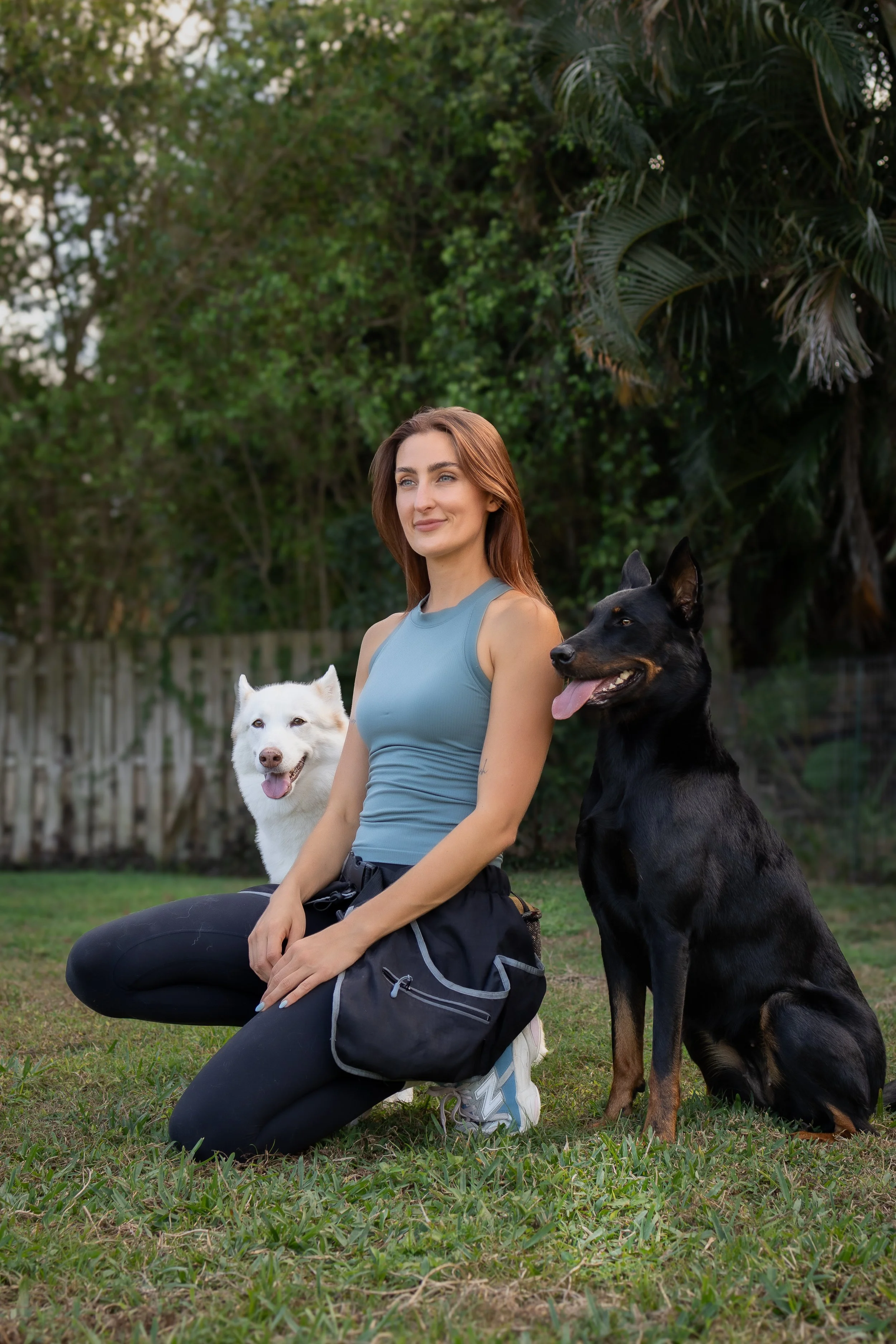 Savanah Lammers, professional dog trainer in Boynton Beach FL, kneeling outdoors with a husky and a Doberman she trained.