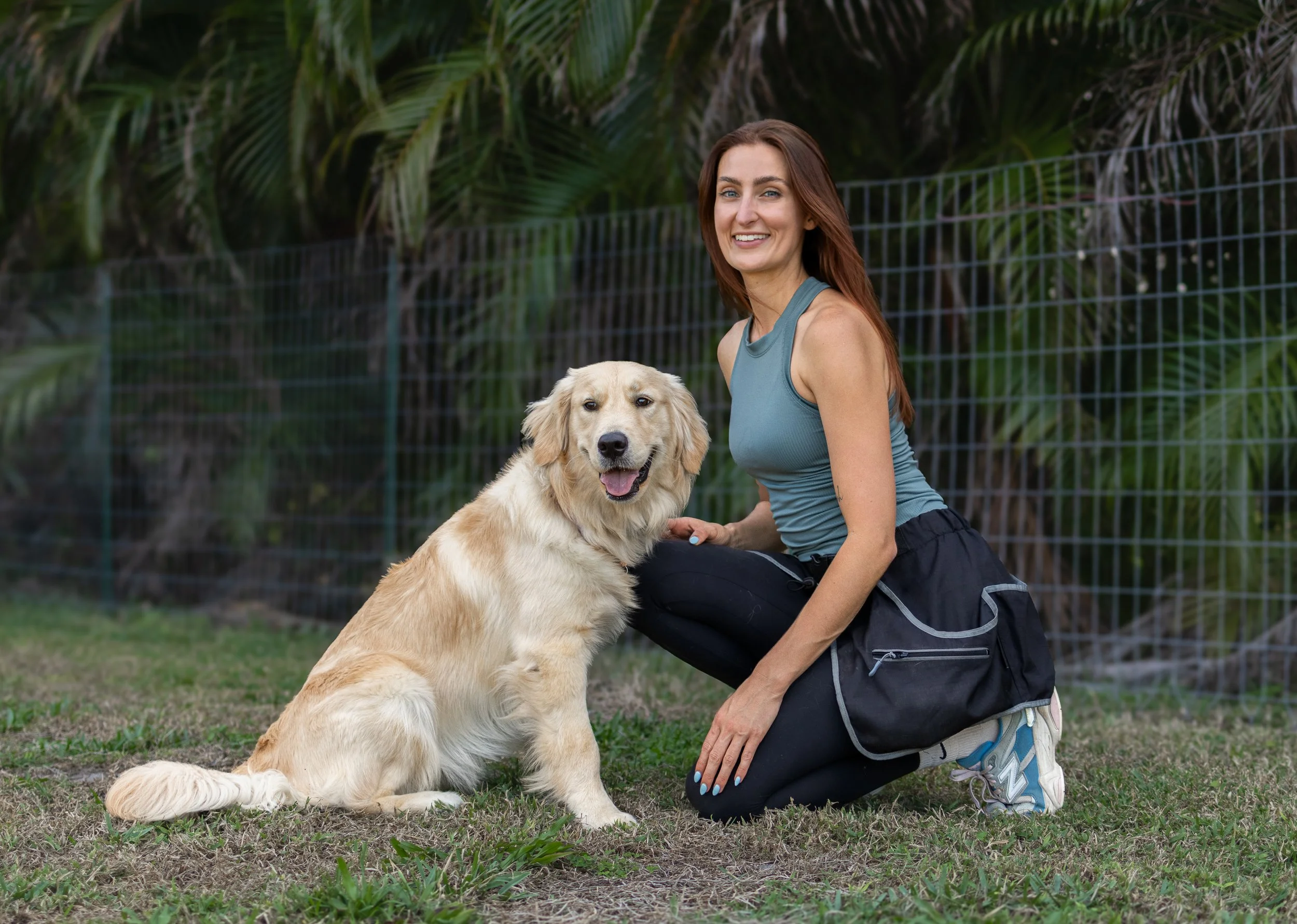 Savanah Lammers, professional dog trainer in Boynton Beach FL, kneeling with a happy golden retriever after a training session