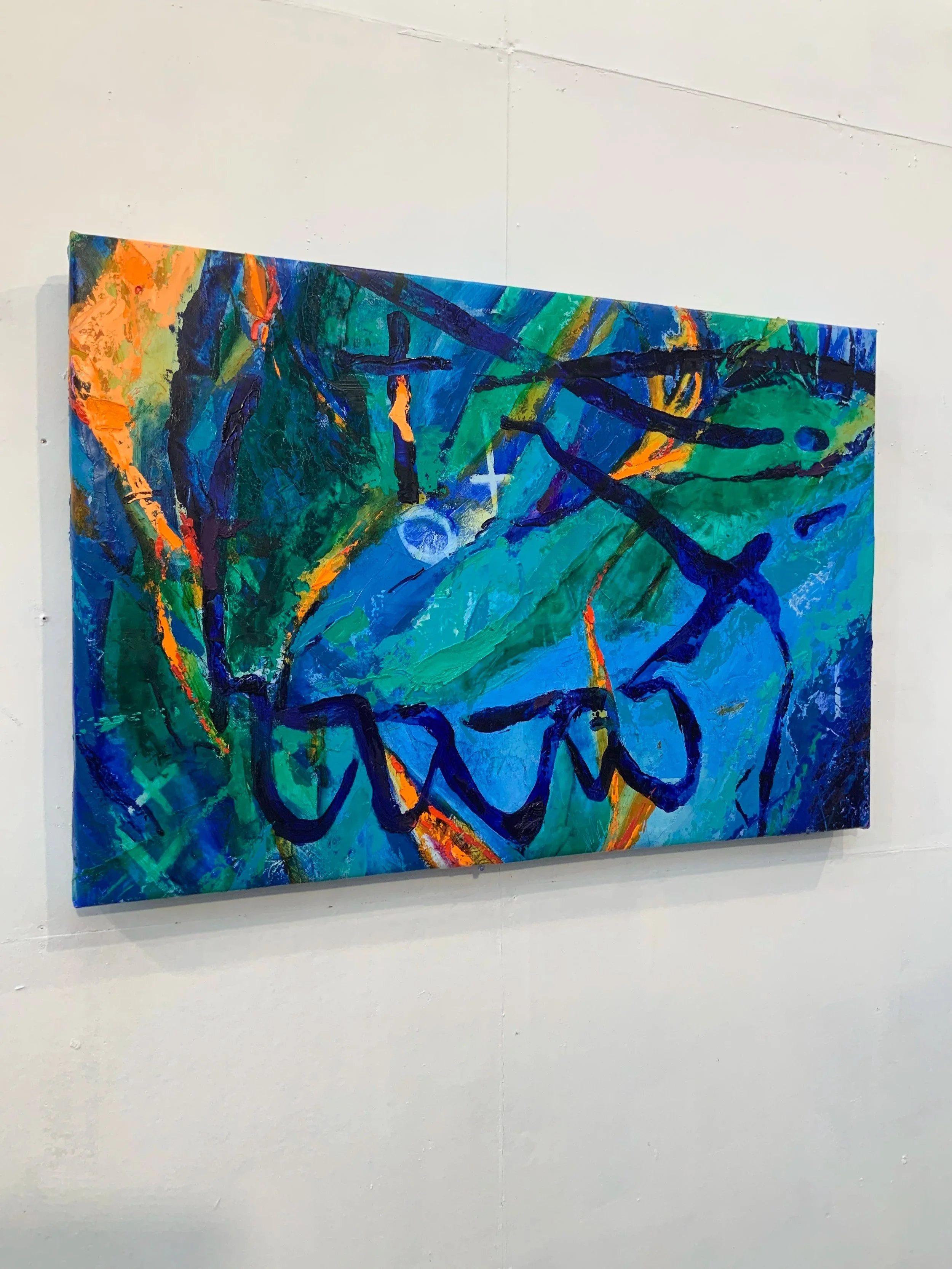 Abstract painting with vibrant blue, green, orange, and black colors and expressive brushstrokes on a white wall.