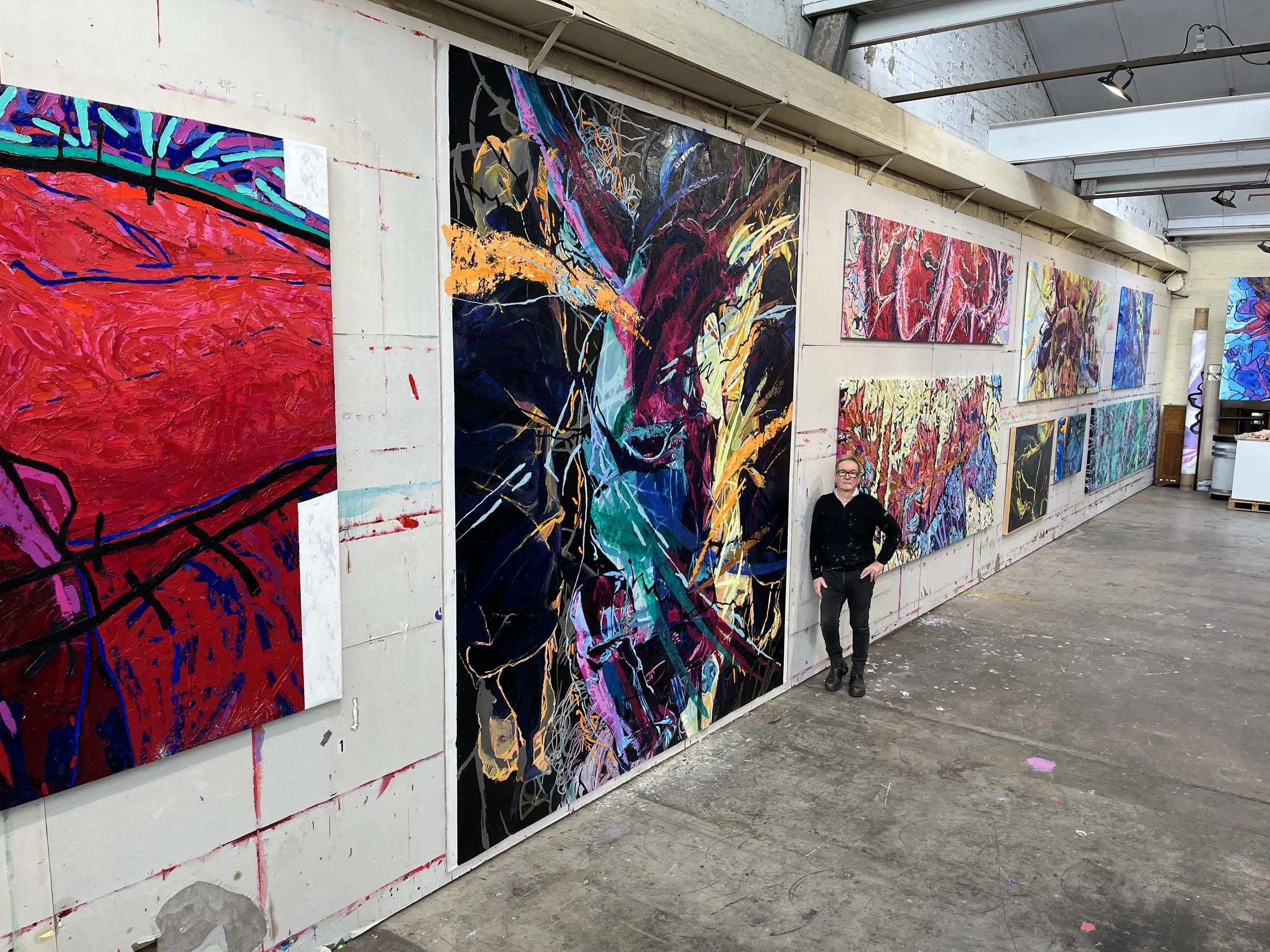 An art gallery with multiple colorful abstract paintings on the wall and a person standing in front of the artwork.