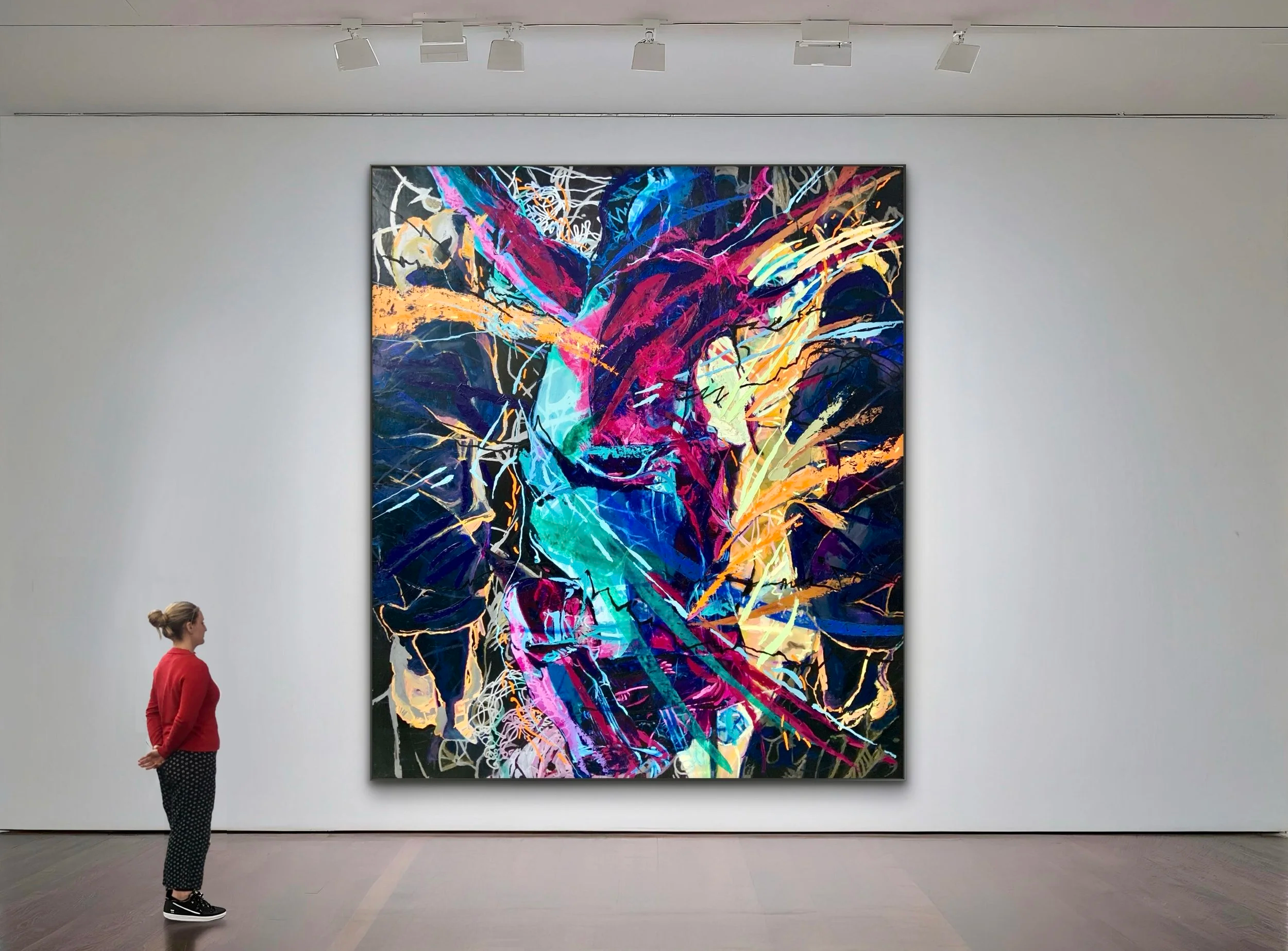 A woman in a red sweater and patterned pants looking at a large, colorful abstract painting in an art gallery.