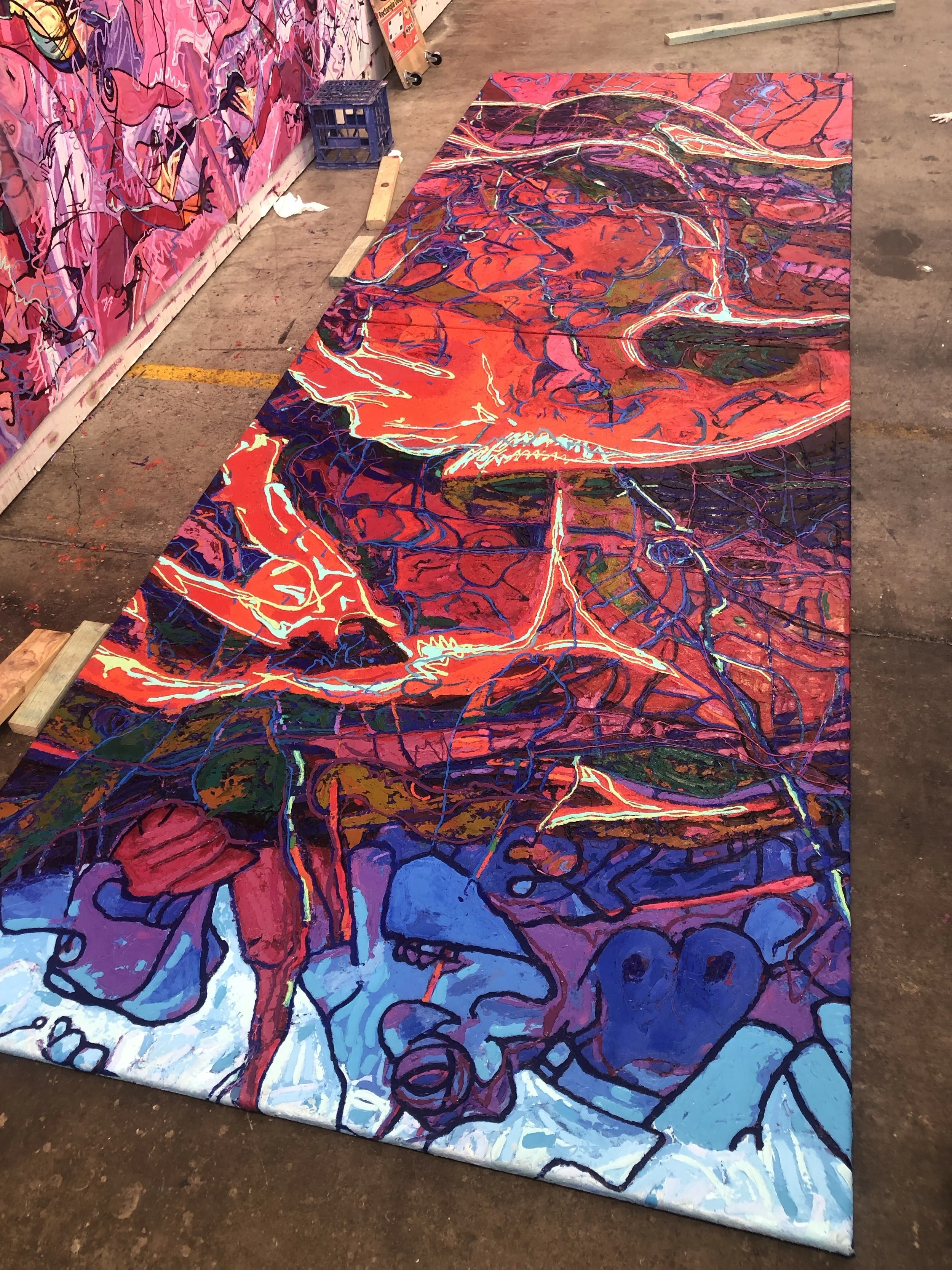 A colorful abstract mural painting on a large canvas laid on the floor, featuring vibrant reds, blues, purples, and orange hues with intricate line work and organic shapes.