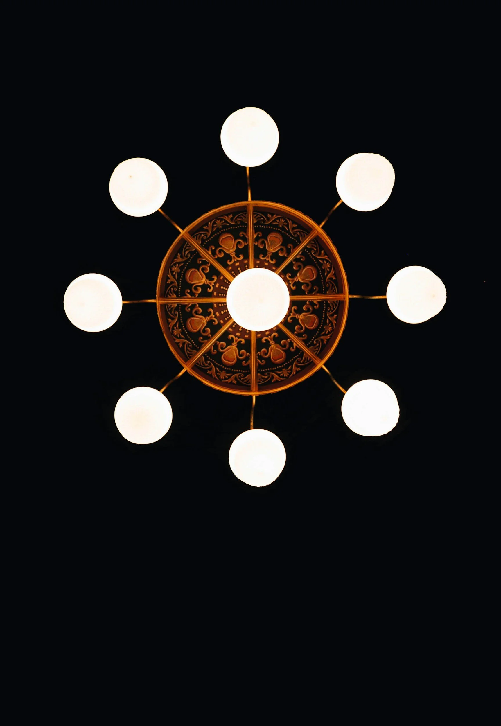 A ceiling chandelier with ten round white bulbs arranged in a circle, set against a black ceiling.