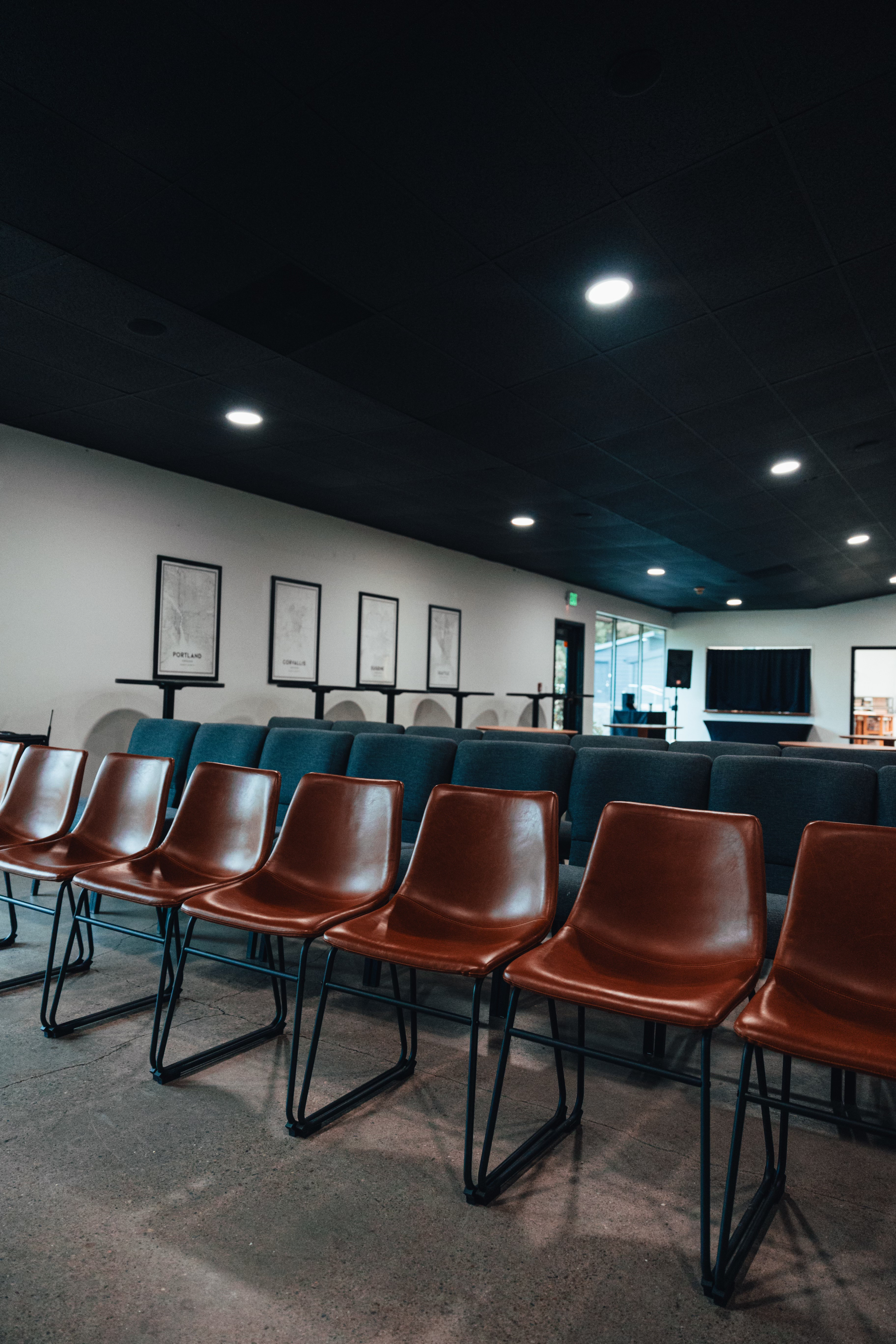 Empty chairs arranged in rows inside a dimly lit conference room or auditorium with framed maps or posters on the wall.