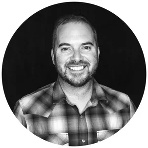Black and white headshot of a smiling man with a beard and short hair, wearing a plaid shirt.