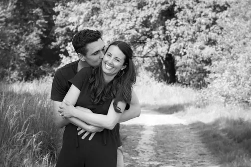 A young couple hugging and smiling outdoors on a grassy path with trees in the background.