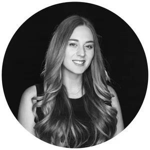 Black and white portrait of a woman with long wavy hair, smiling, set against a dark background.