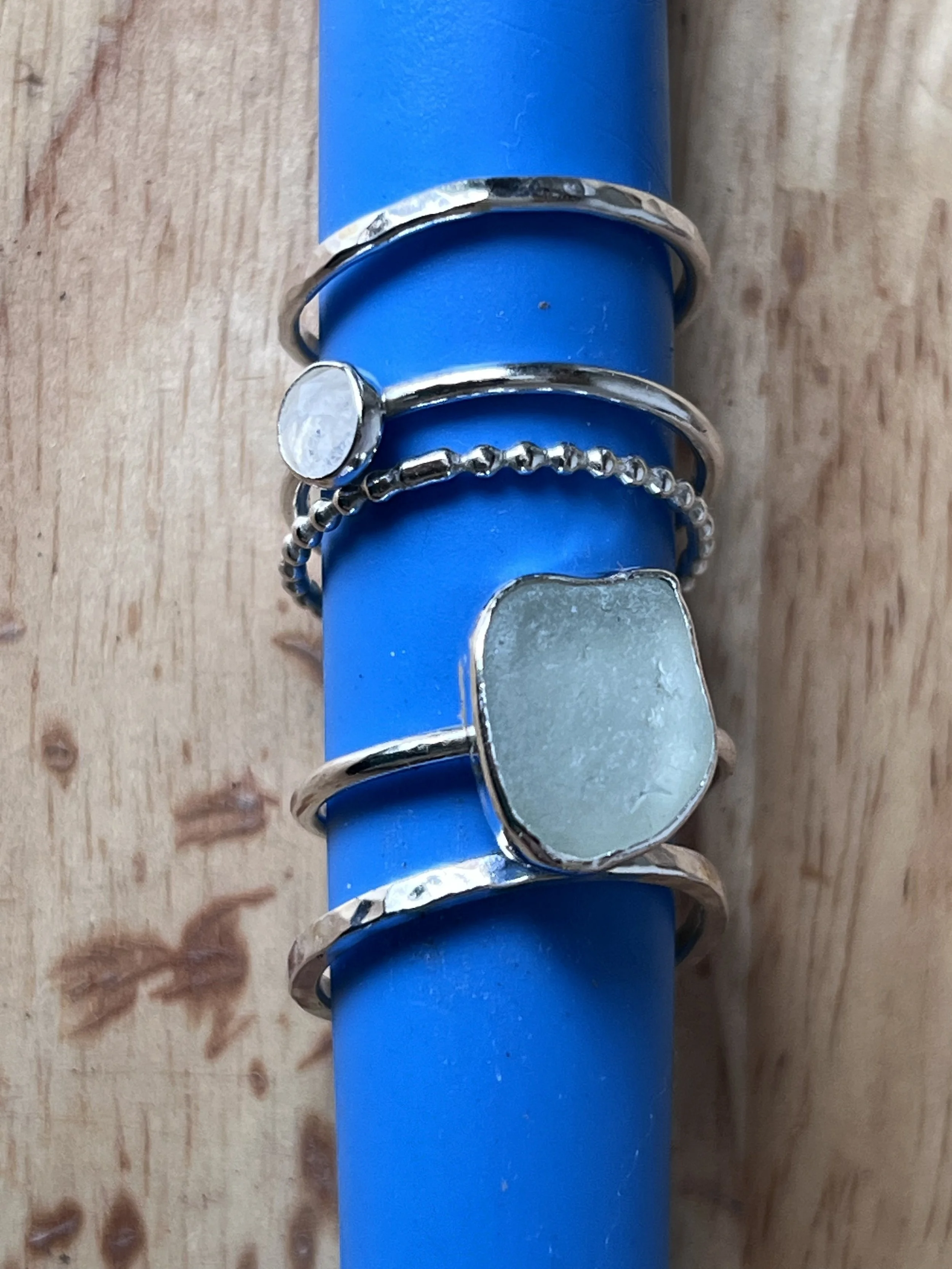 Four silver rings with different designs and stones, placed on a blue cylindrical object.