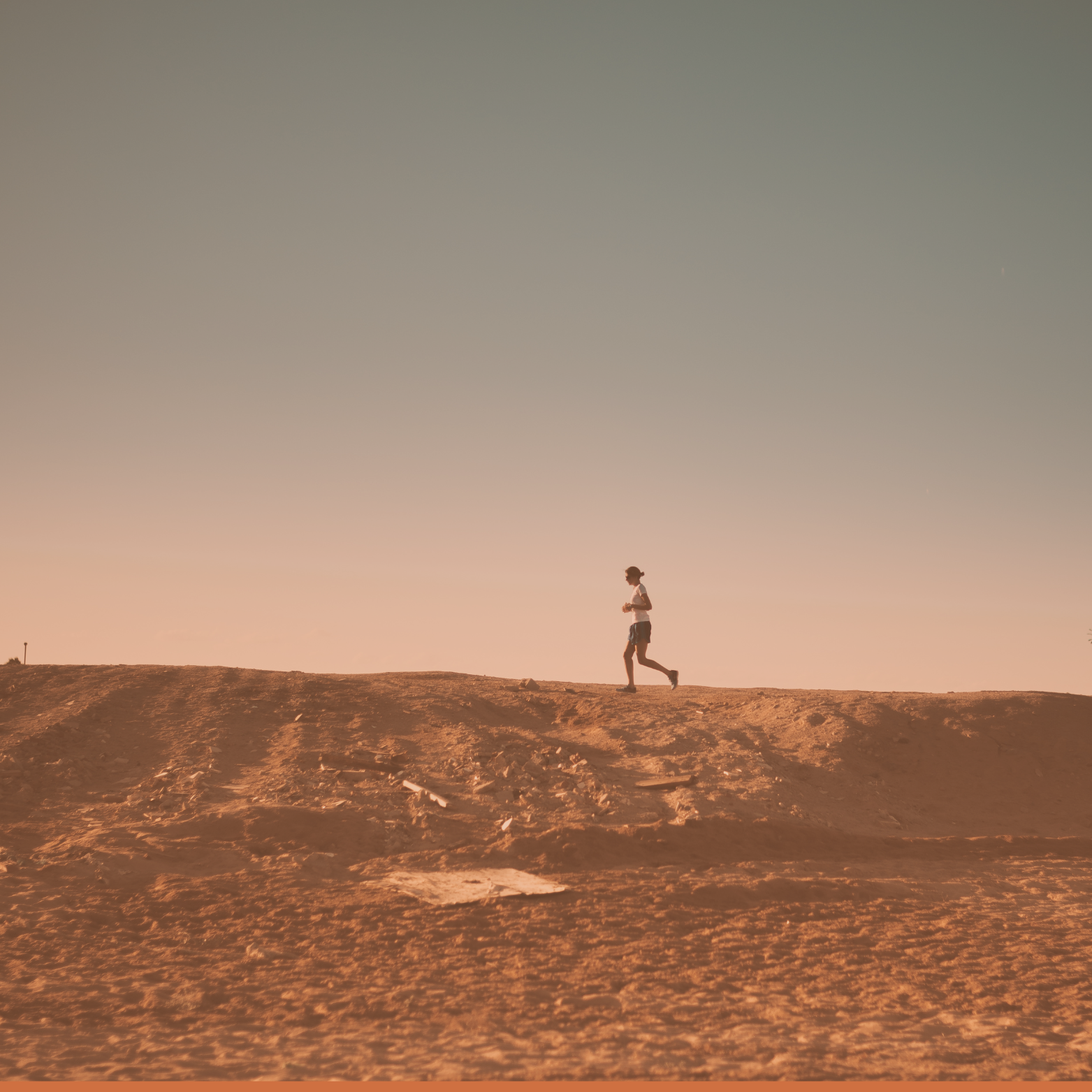 A person running along a dirt path at sunset, with a clear sky in the background.