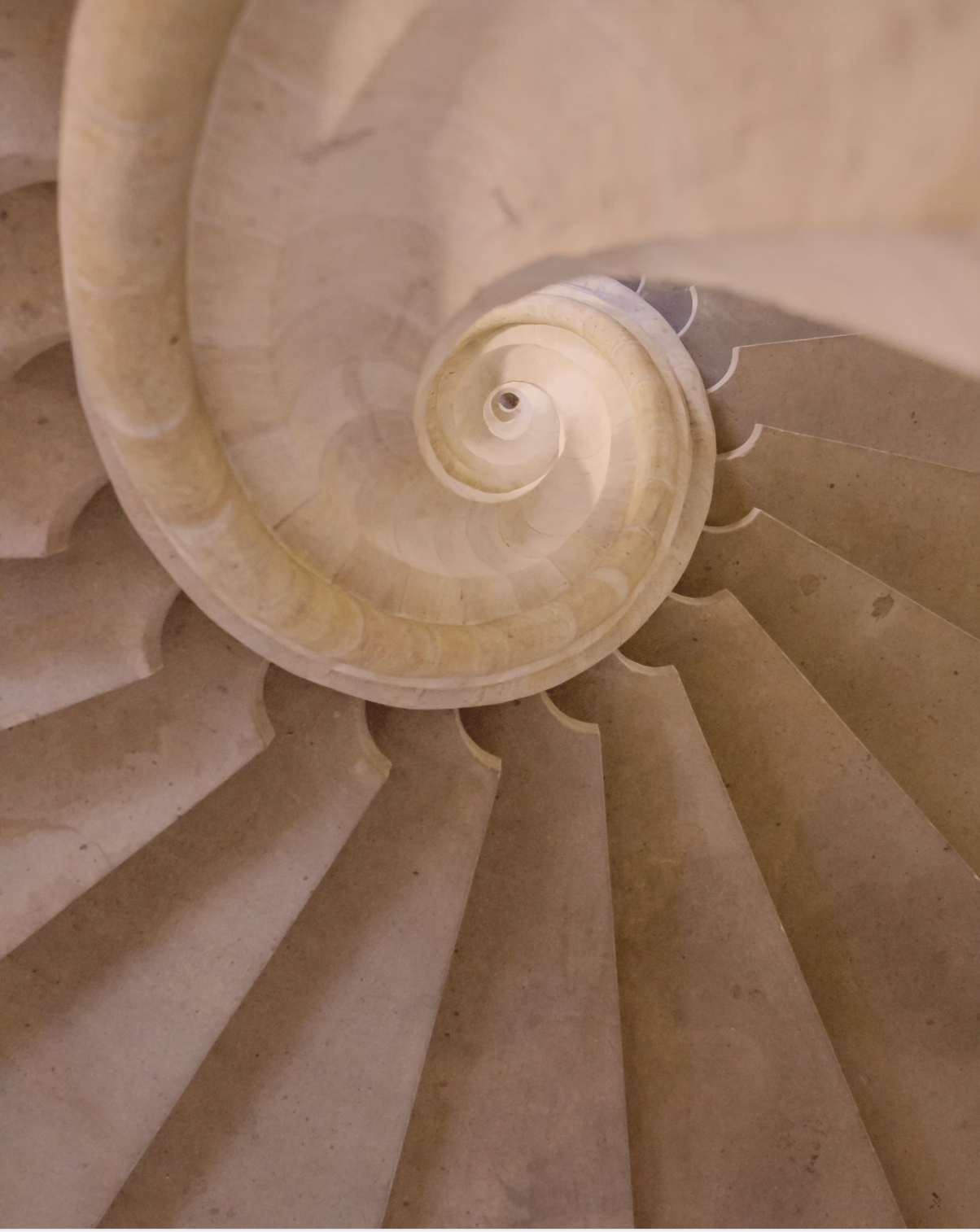 Top-down view of a spiral staircase made of beige stone, tapering towards the center.