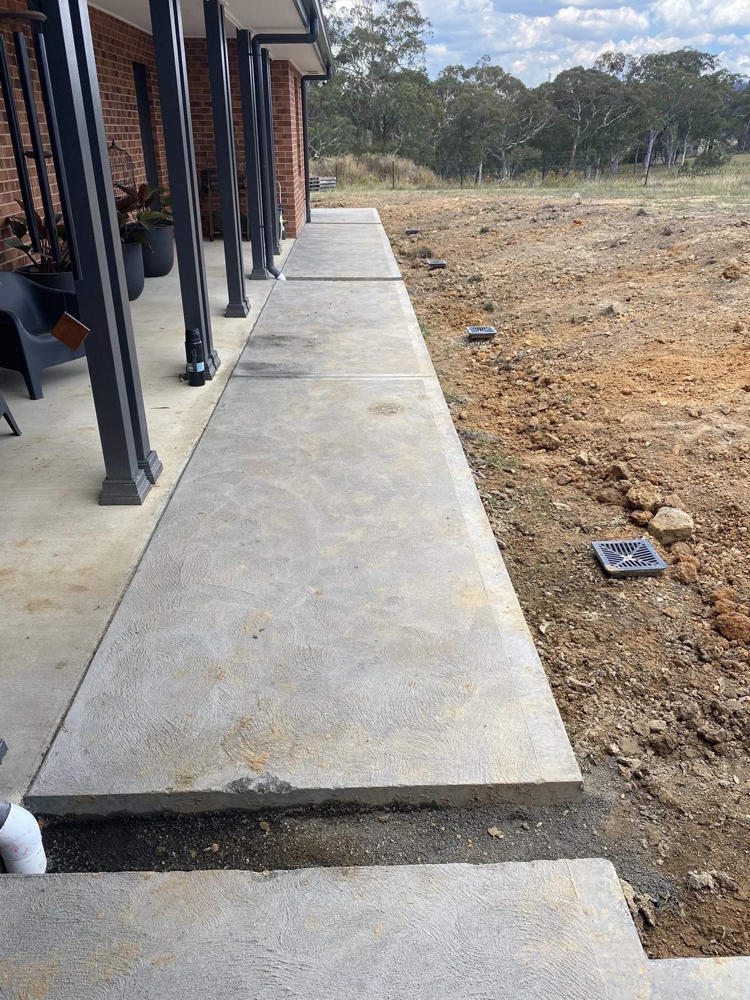 Drainage channel running alongside a concrete footpath and the foundation of a new brick home.
