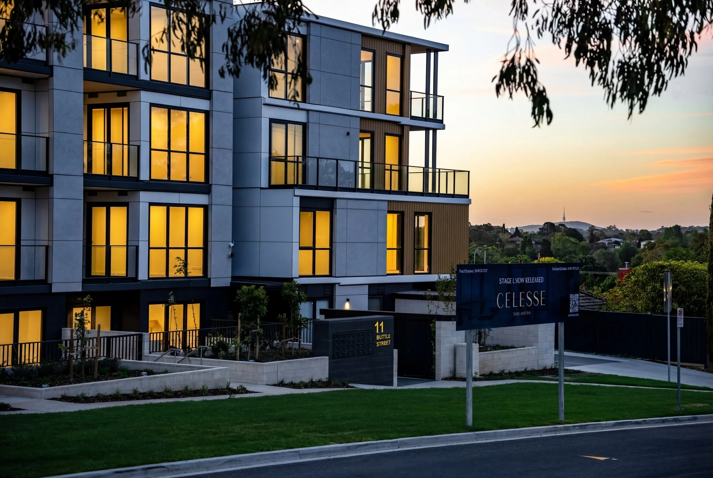 Modern multi-story apartment building with illuminated windows at sunset, surrounded by landscaped greenery, with a street sign reading '11 Buttle Street' and a billboard advertising 'Celesse' in the foreground.