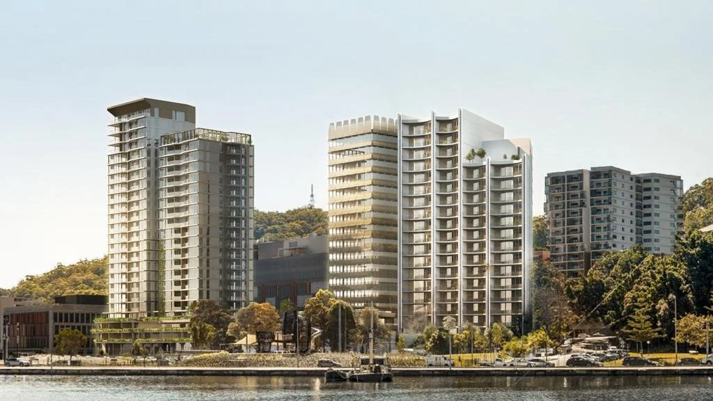 Modern high-rise buildings line a waterway with trees and a hill in the background.