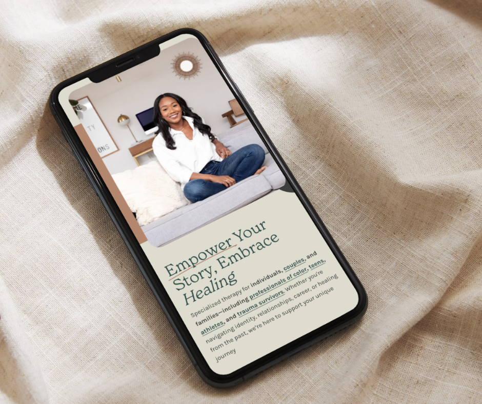 Smartphone displaying a website about empowerment and healing, with a smiling woman sitting cross-legged on a couch in the background.
