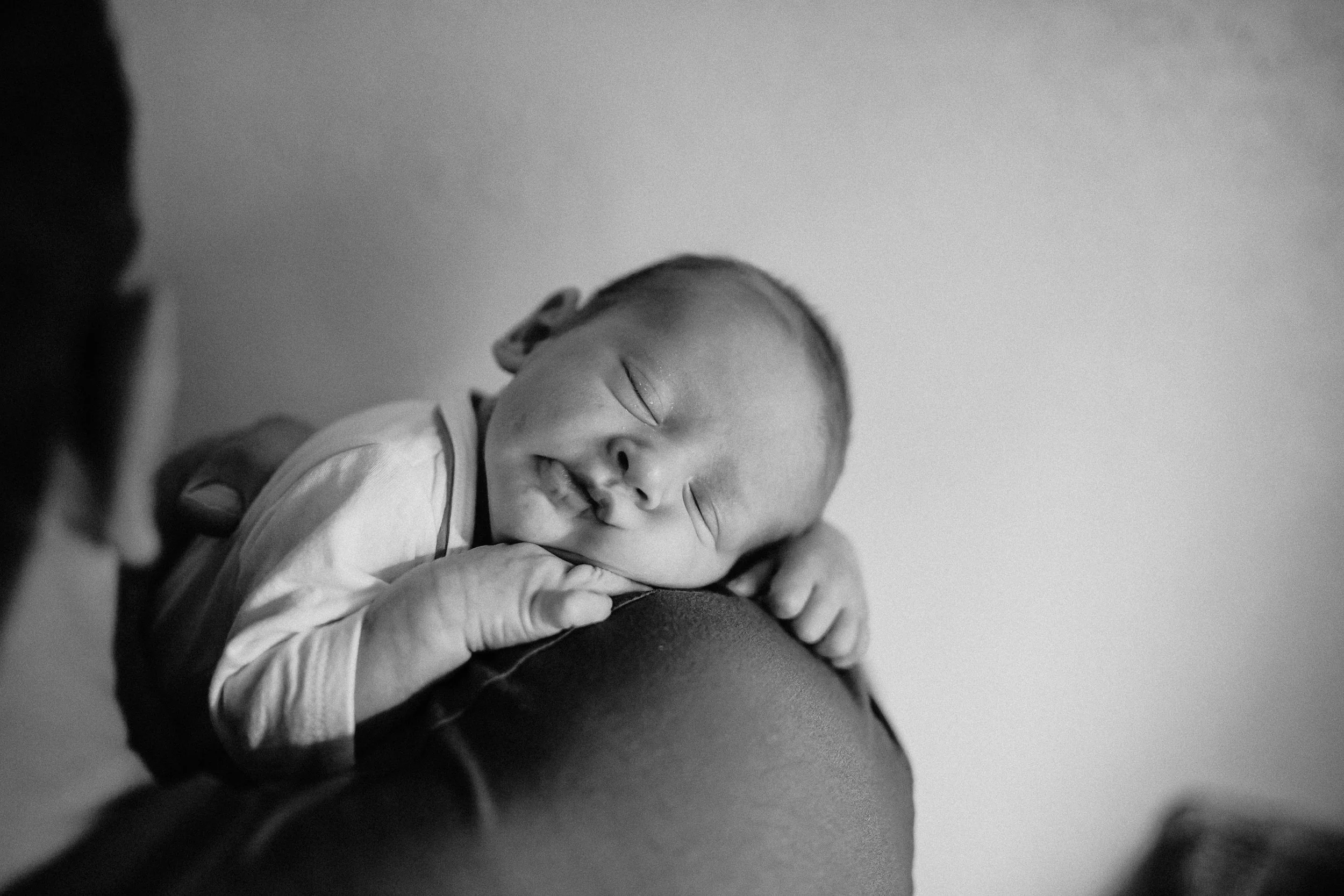 Black and white photo of a newborn baby sleeping peacefully on someone's shoulder, with a gentle smile, closed eyes, and an arm wrapped around the person's neck.