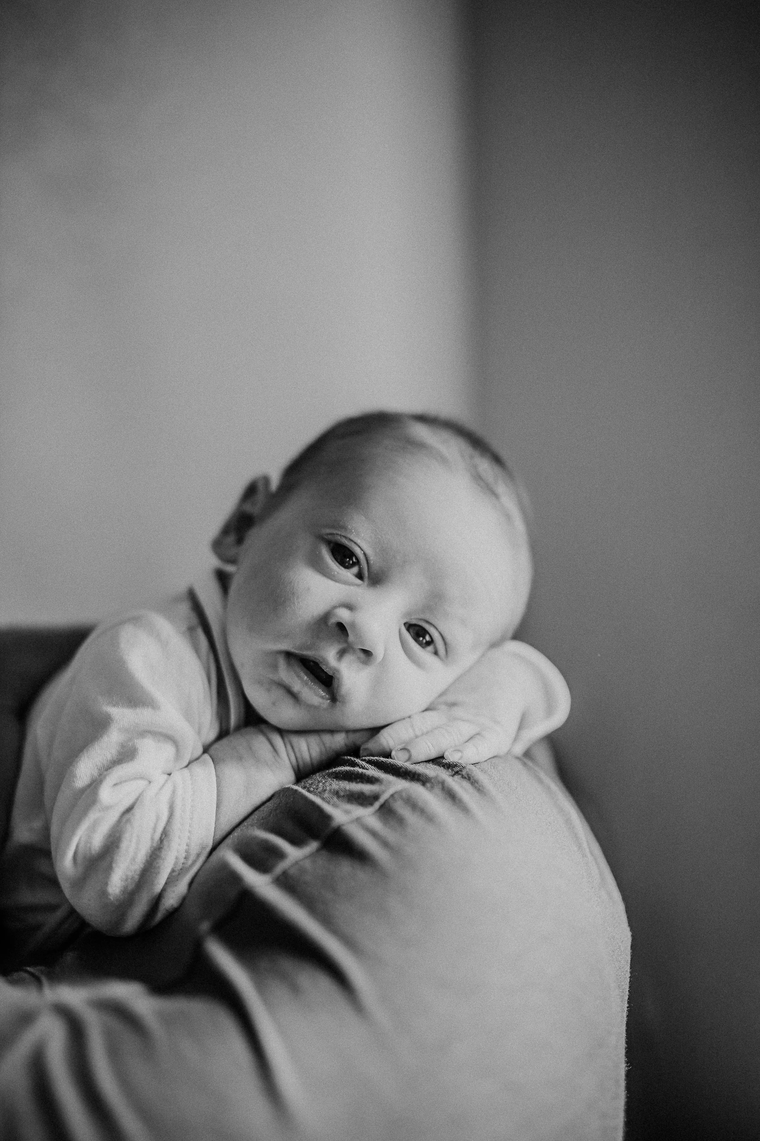 Black and white photo of a young child resting their arms on a soft surface, looking directly at the camera.
