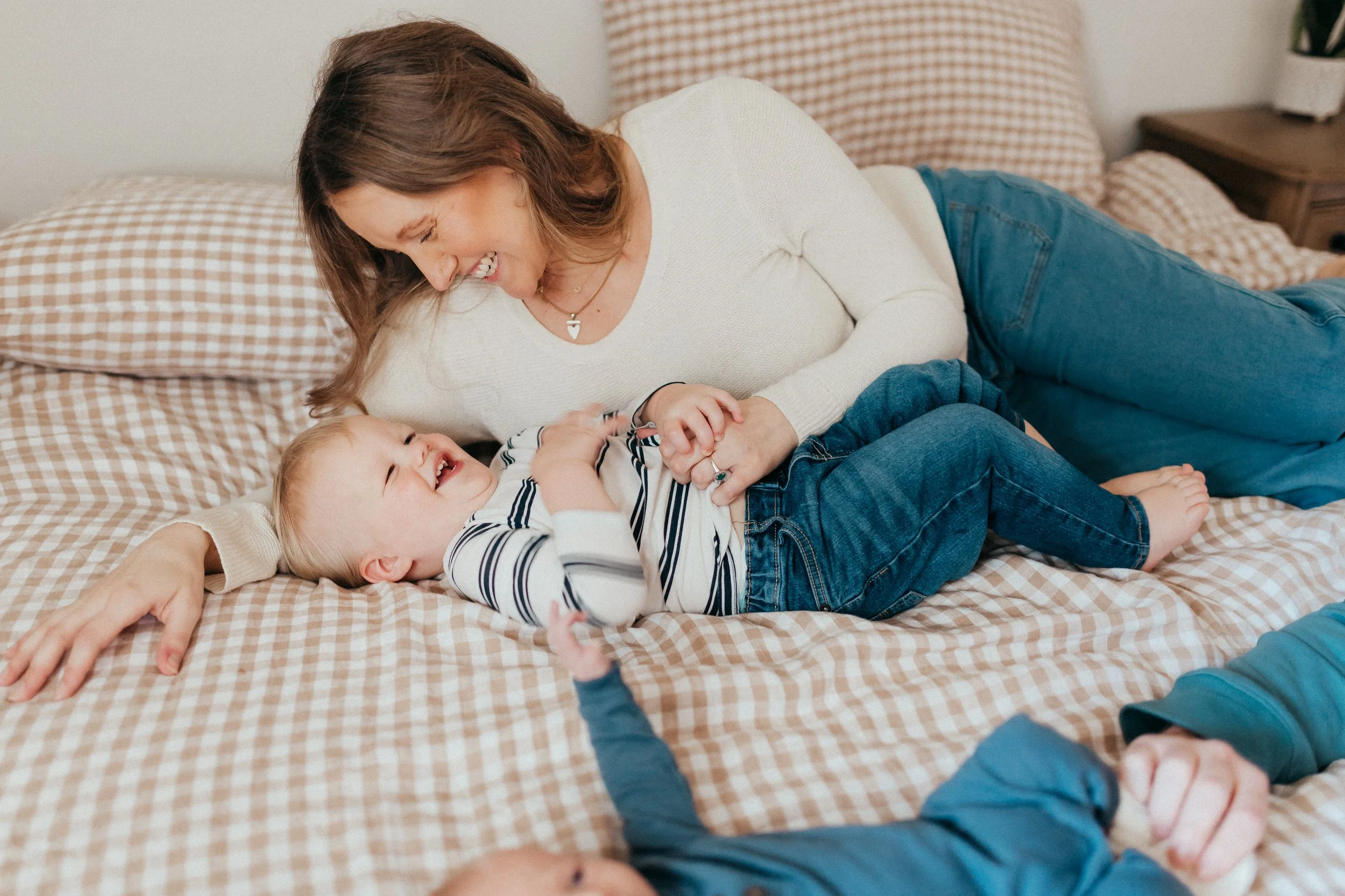 A woman and a young boy playing and laughing together on a bed with a checkered blanket.