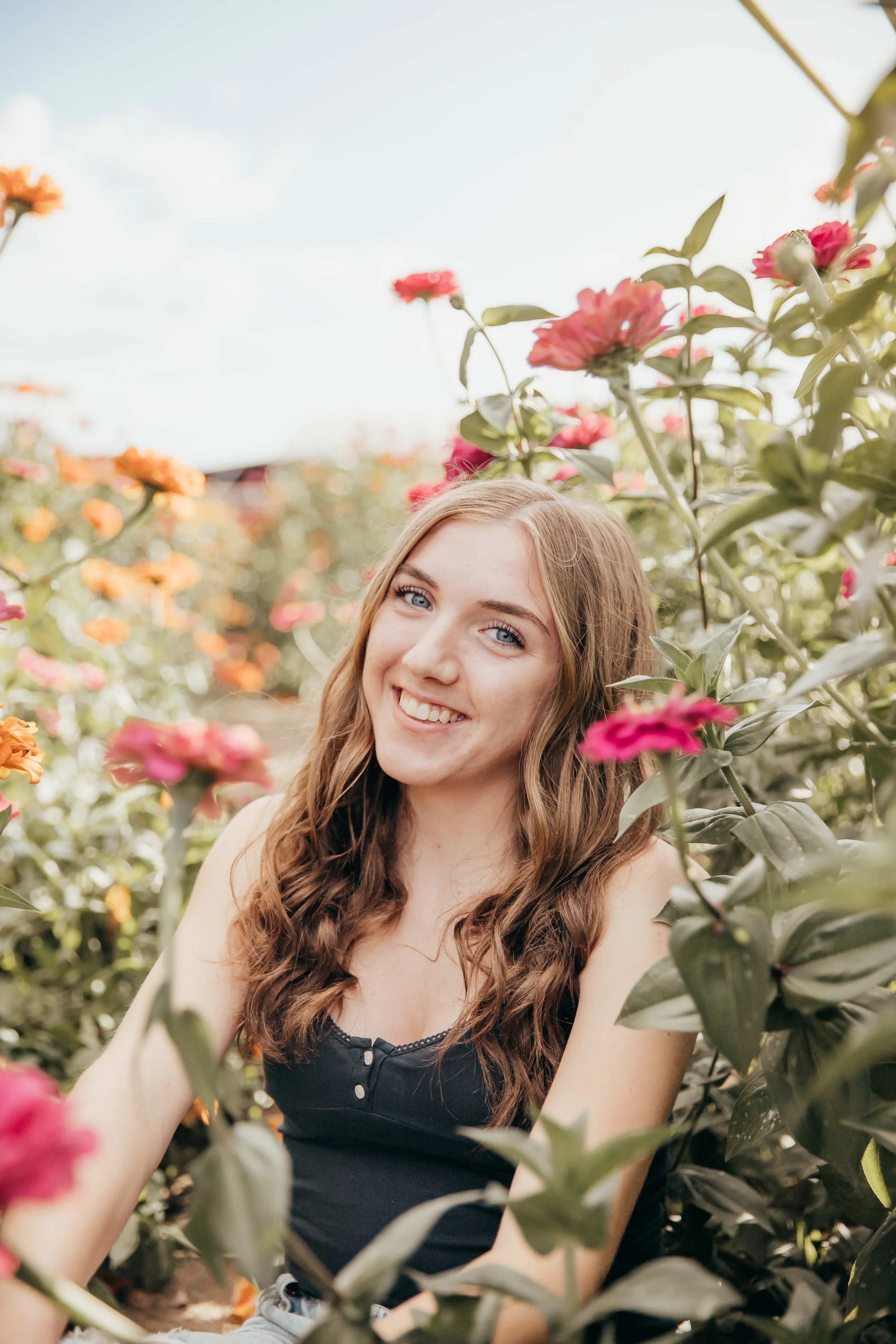 A young woman smiling among pink and orange flowers outdoors.
