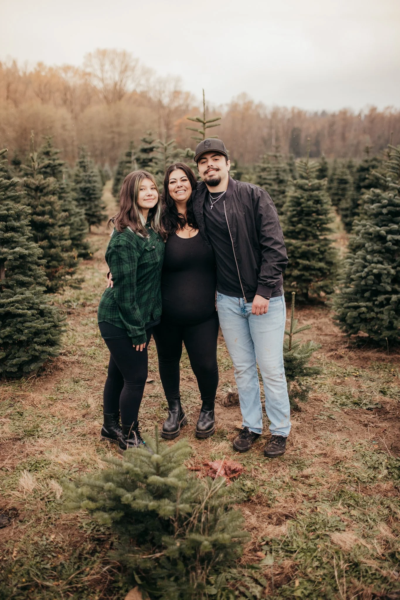 A family of three standing together in a Christmas tree farm