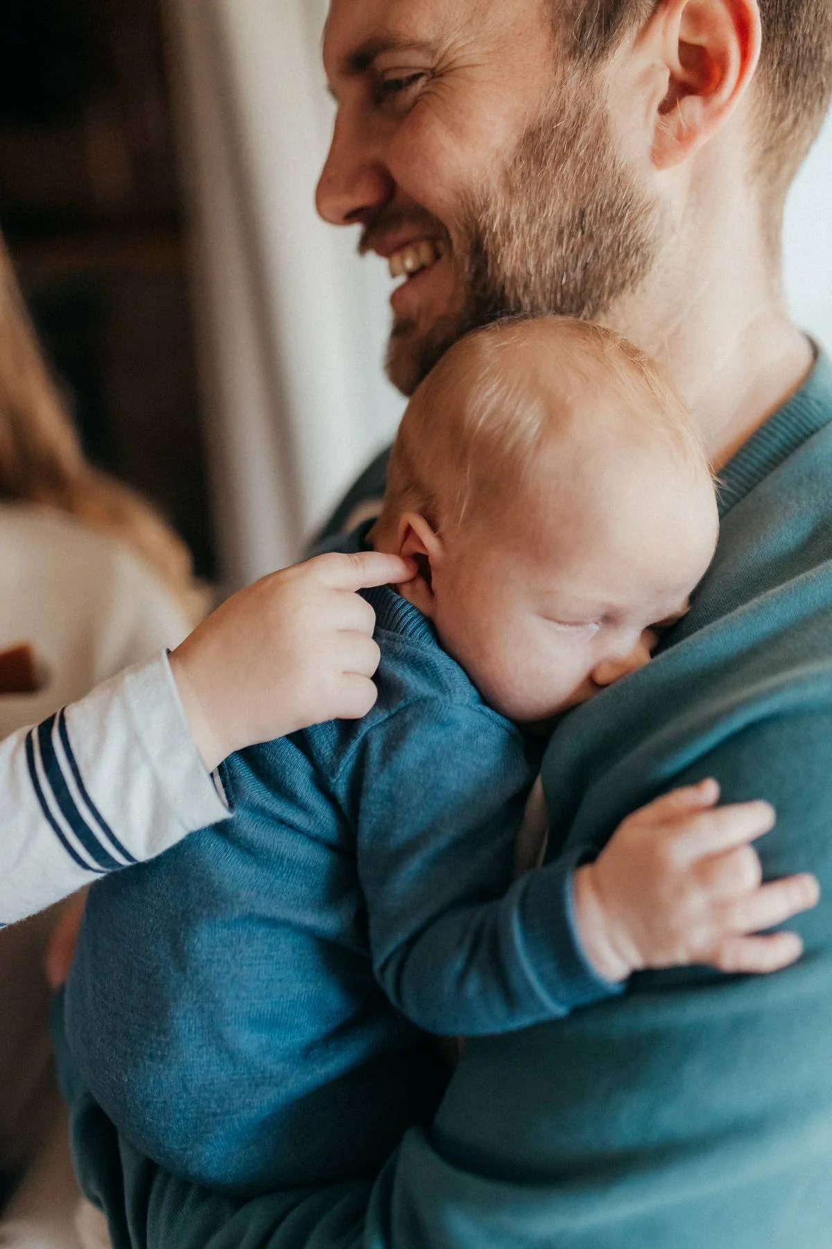 A man with a beard smiling while holding a young child with red hair, who is resting their head on his shoulder and touching his ear.