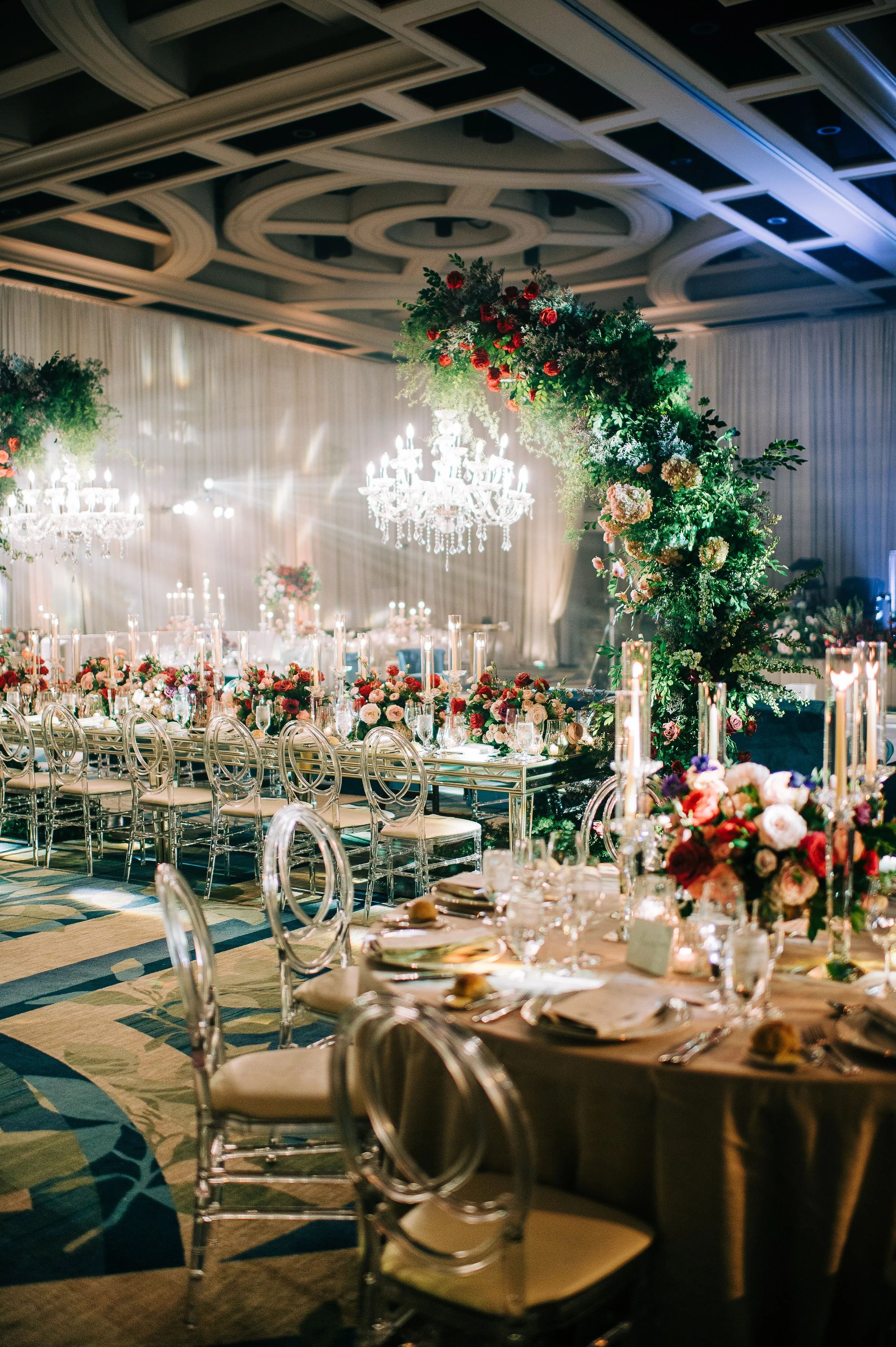 Elegant banquet hall decorated with floral arrangements, candles, and a chandelier, set for a formal event or wedding reception.