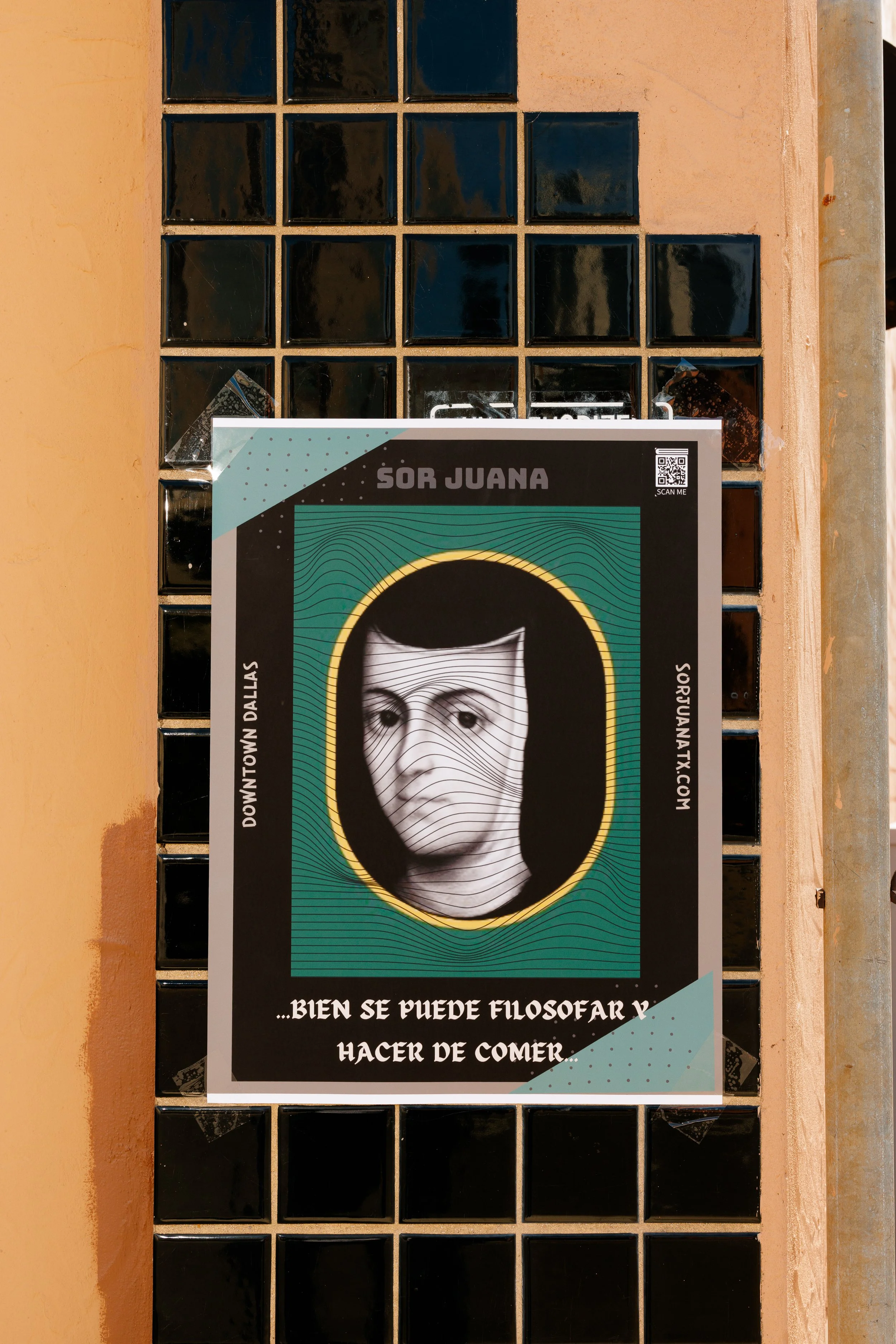 A poster featuring a black and white portrait of a woman with a serious expression, framed by a yellow outline, on a teal background with wave patterns. The poster includes text in Spanish, the website URL, a QR code, and is attached to a wall with glass blocks.