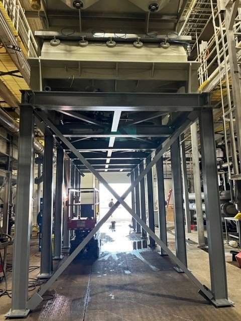 Industrial machinery with a metal frame and large equipment on top, inside a factory or plant.