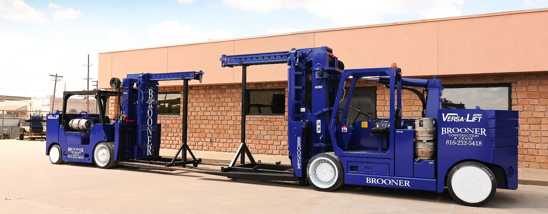 Blue construction lift truck parked outside a brick building with windows and a pink upper wall