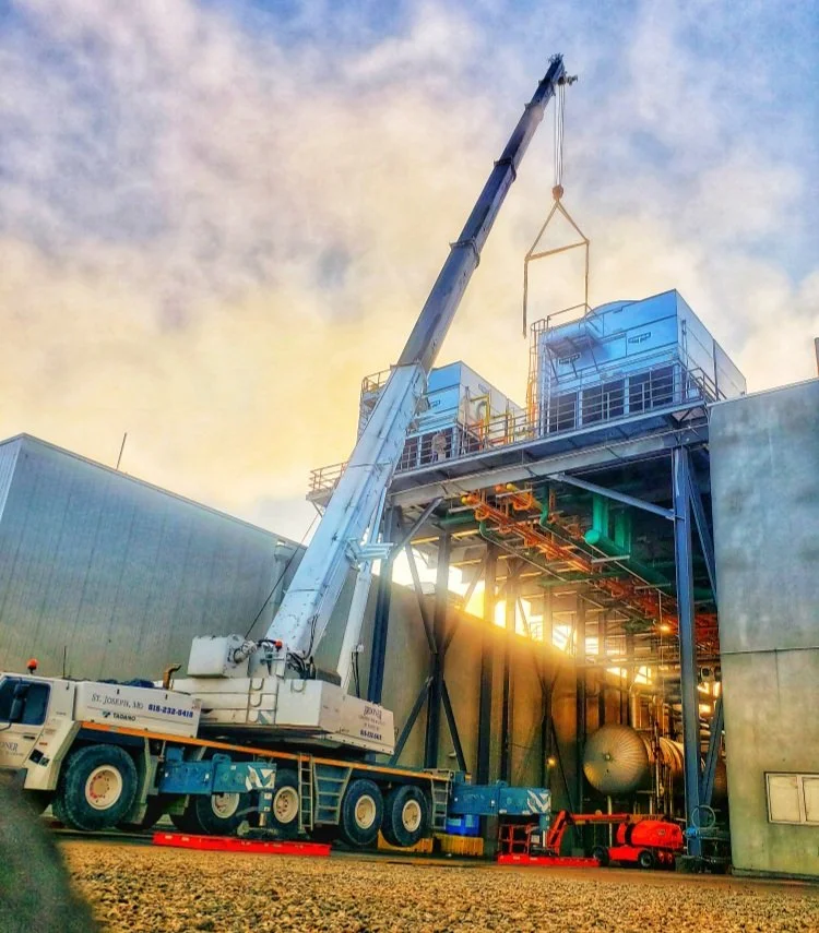 A construction crane lifting equipment onto an industrial building at sunset.