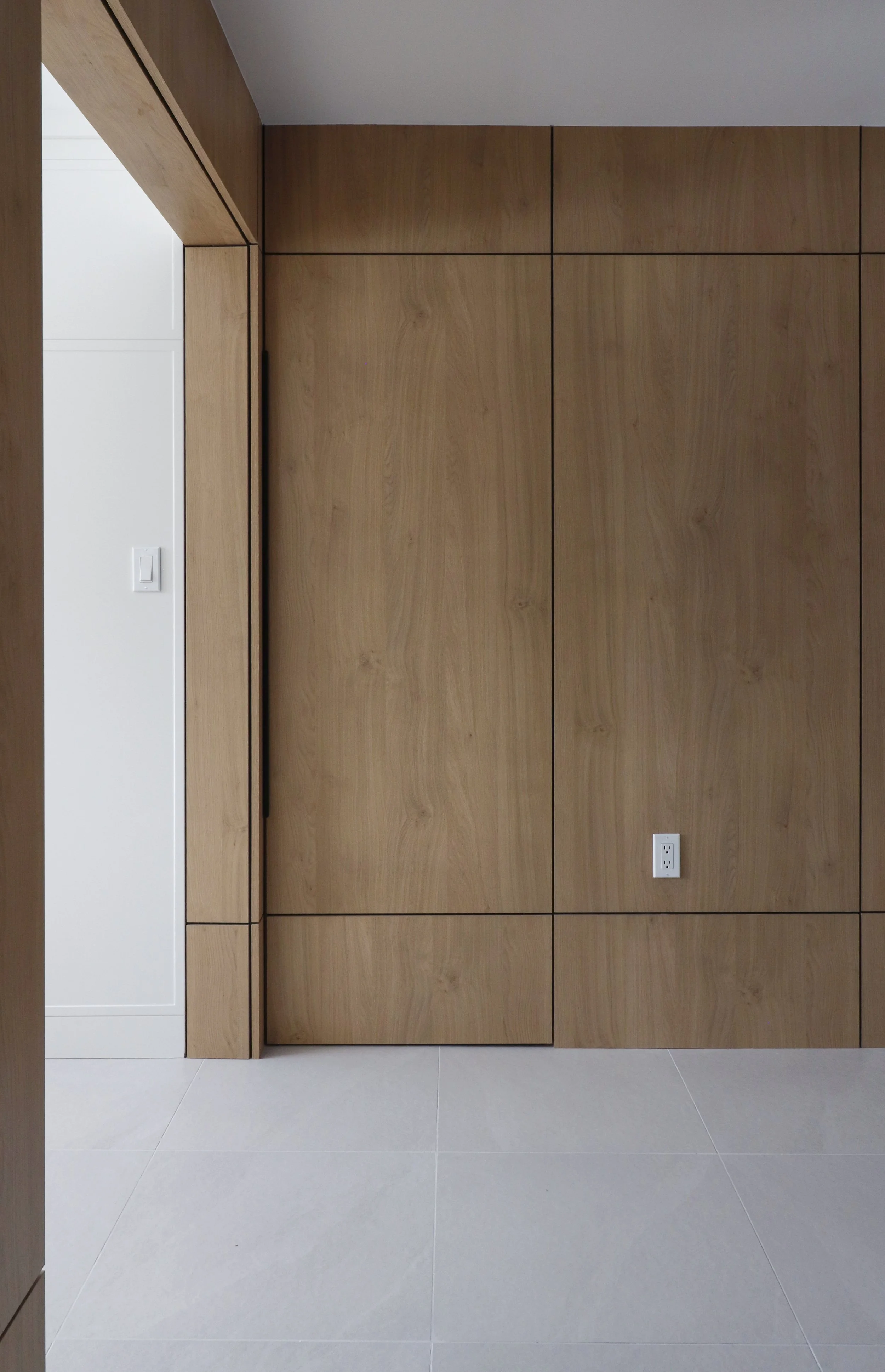A modern interior wall with wooden panels and white tile flooring, featuring electrical outlets and a light switch.