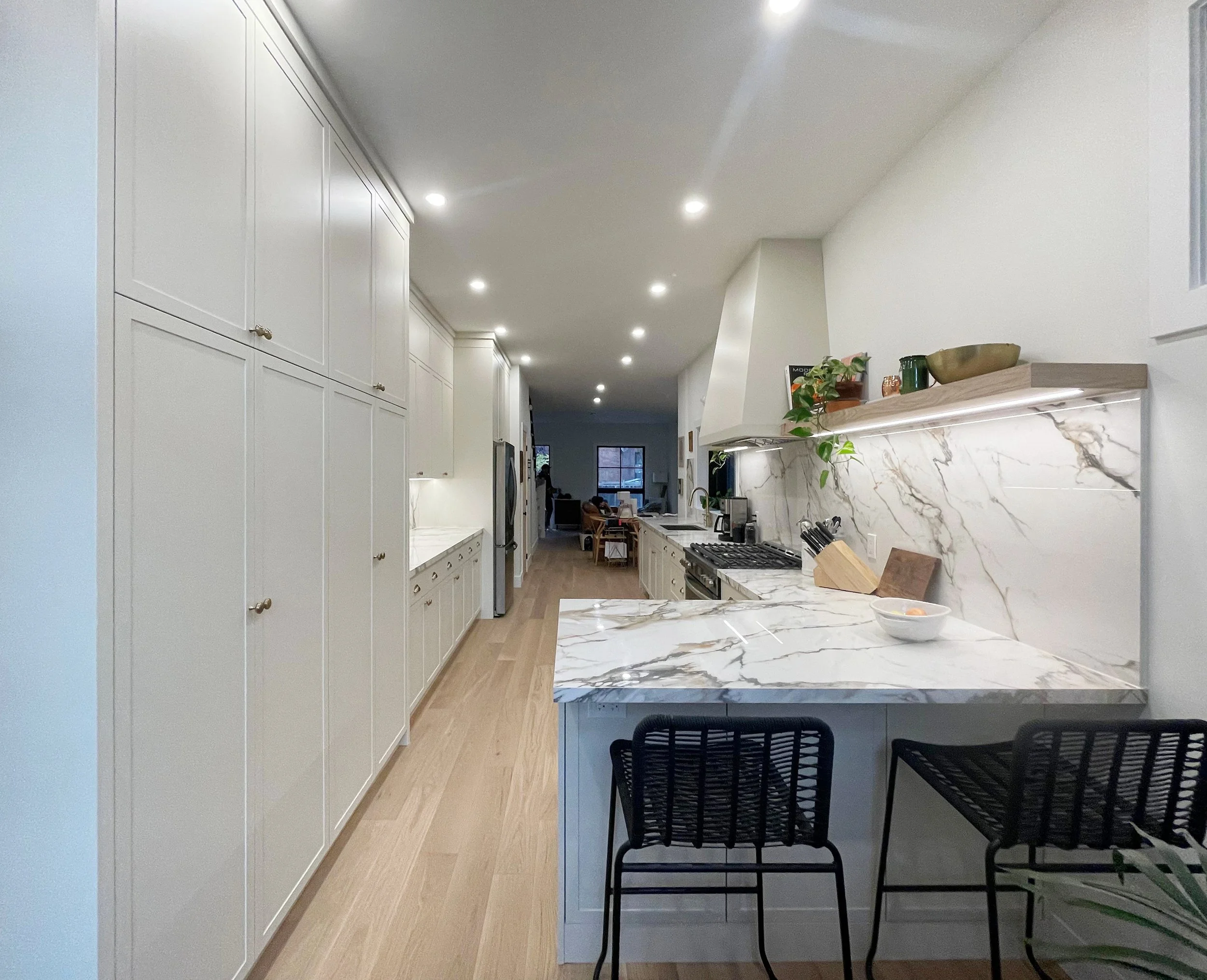 Modern kitchen with white cabinets, marble countertops, black dining chairs, built-in appliances, and recessed lighting.