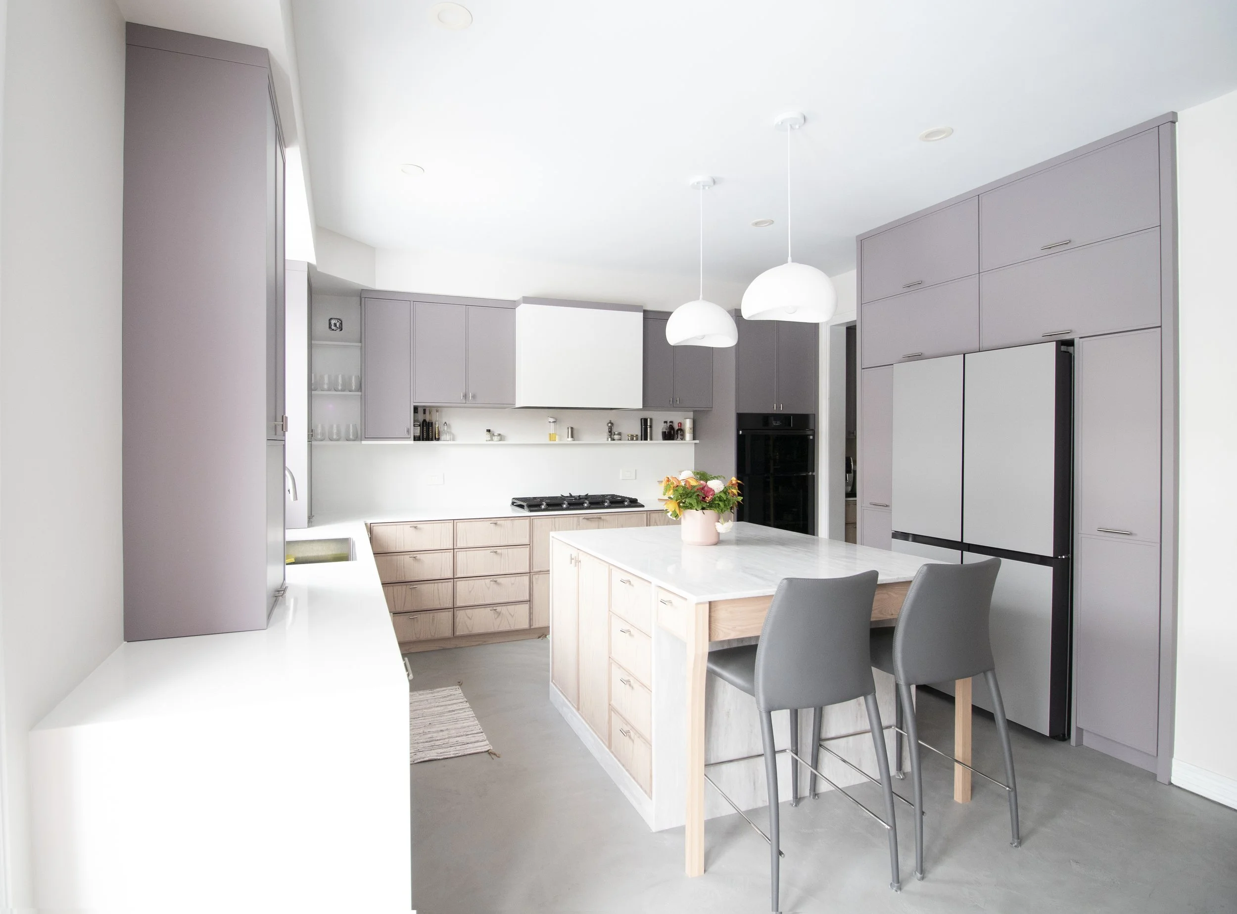 Modern kitchen with gray cabinets, white countertops, and a central island with gray chairs, pendant lights, and a flower arrangement on the island.
