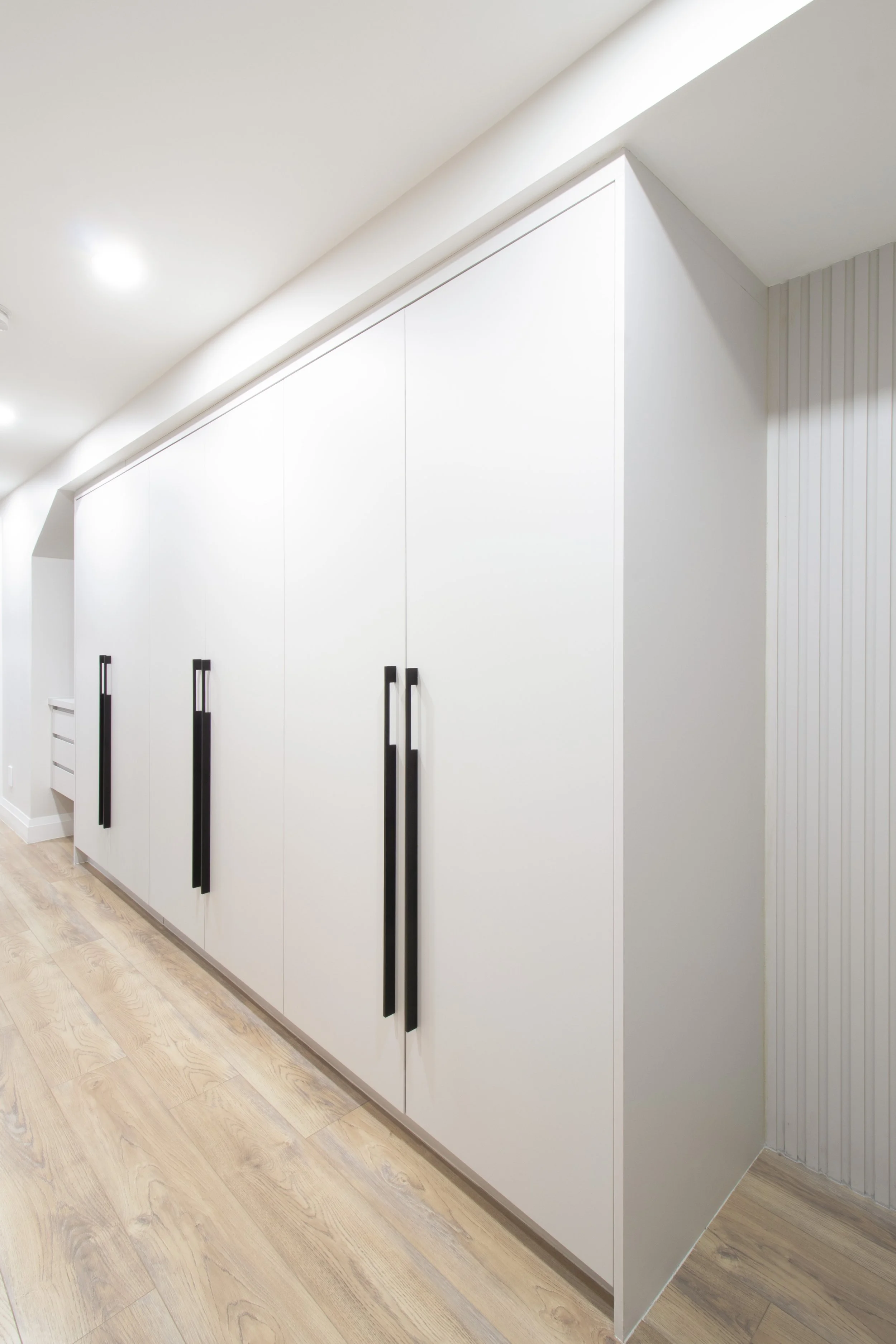 White built-in closet with black handles in a room with light wooden flooring and white walls.