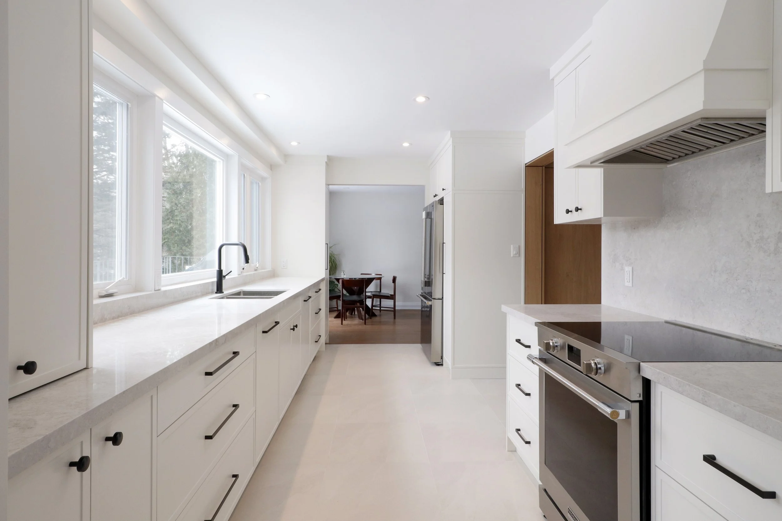 Modern kitchen with white cabinets, marble countertops, stainless steel appliances, and large windows letting in natural light.