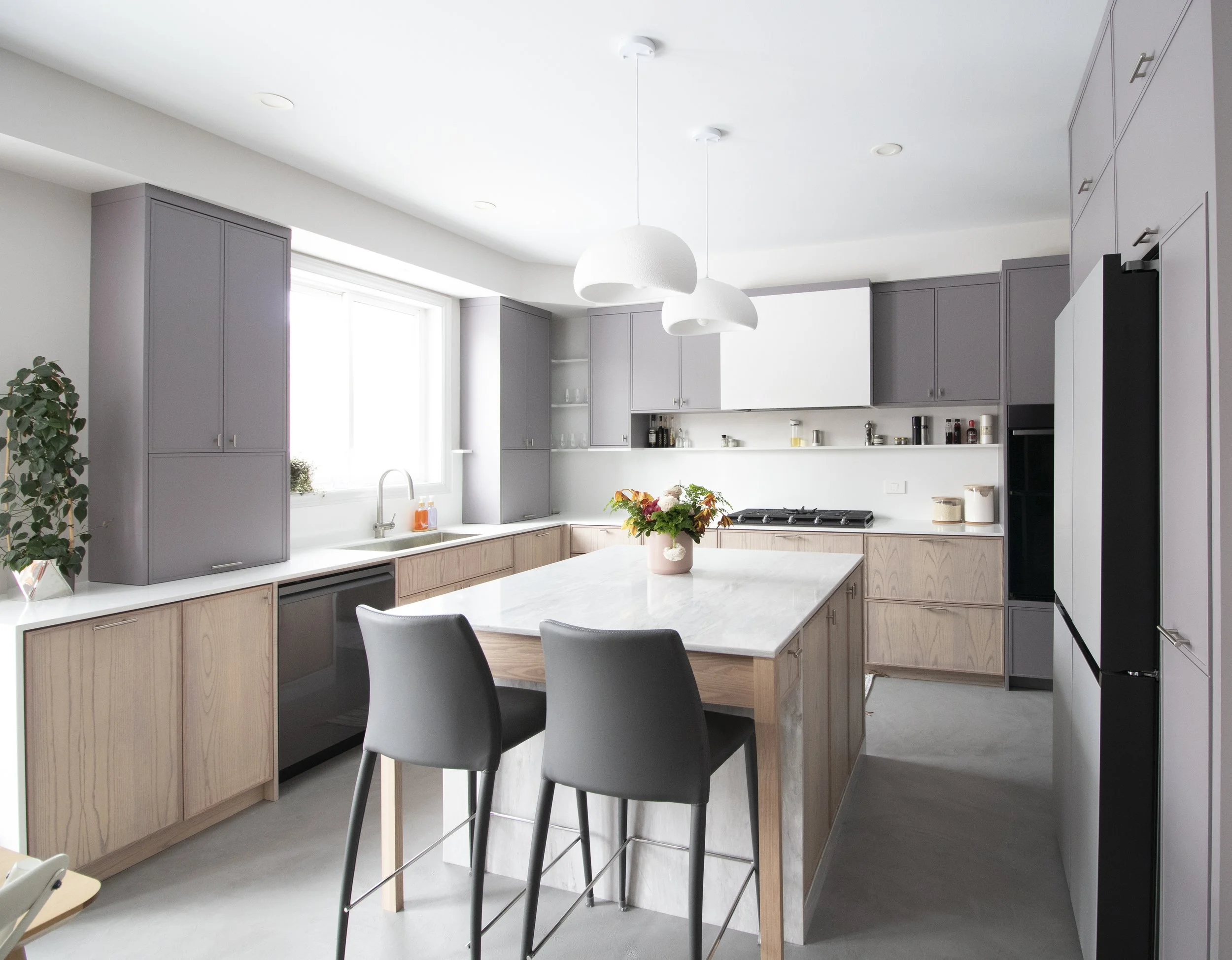 Modern kitchen with gray cabinets, white countertops, and a central island, decorated with a vase of flowers, under white pendant lights.