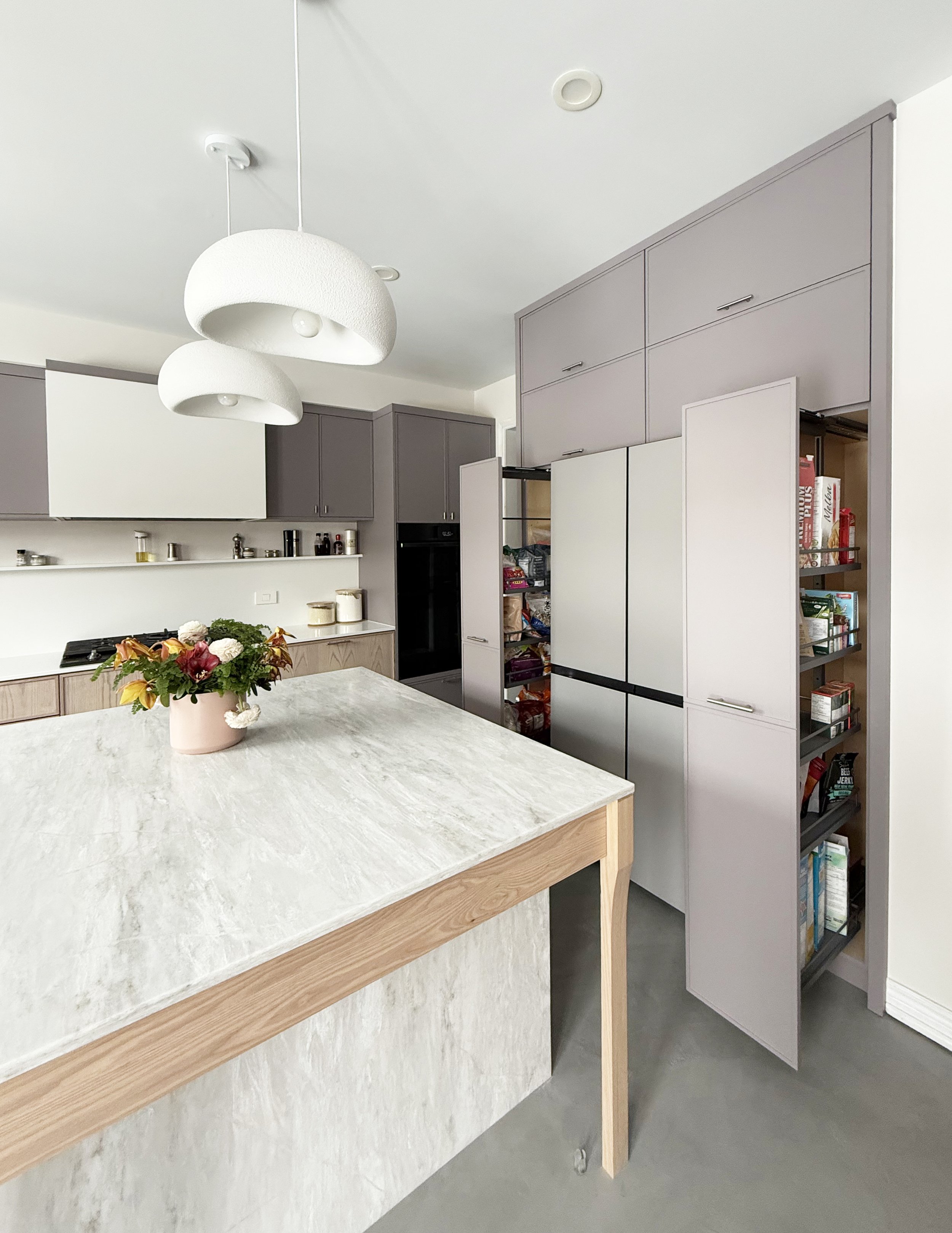 A modern kitchen with light wood and white cabinetry, a marble kitchen island, and pendant lights hanging from the ceiling.
