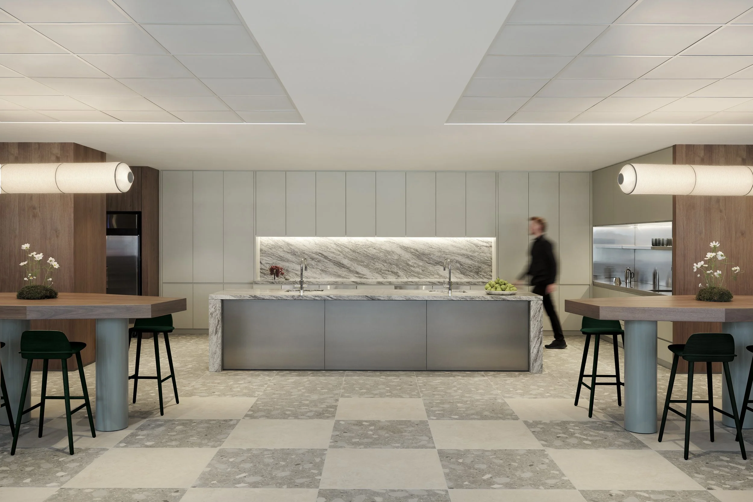 Modern kitchen with marble island, white cabinetry, wooden accents, and a person walking past.