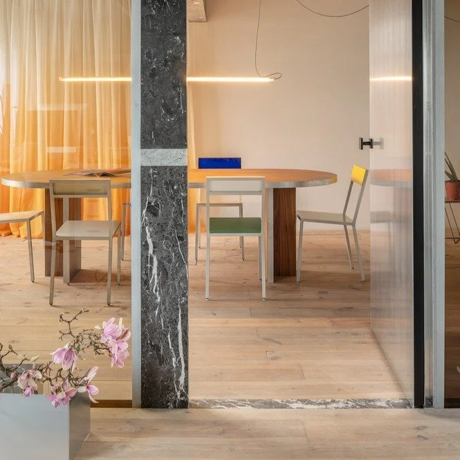 This office was designed to work with the existing materials in the space, including the brightly colored exposed pipes. &quot;The color palette in the meeting room was chosen to complement the existing hues: yellow for gas and green for electricity.