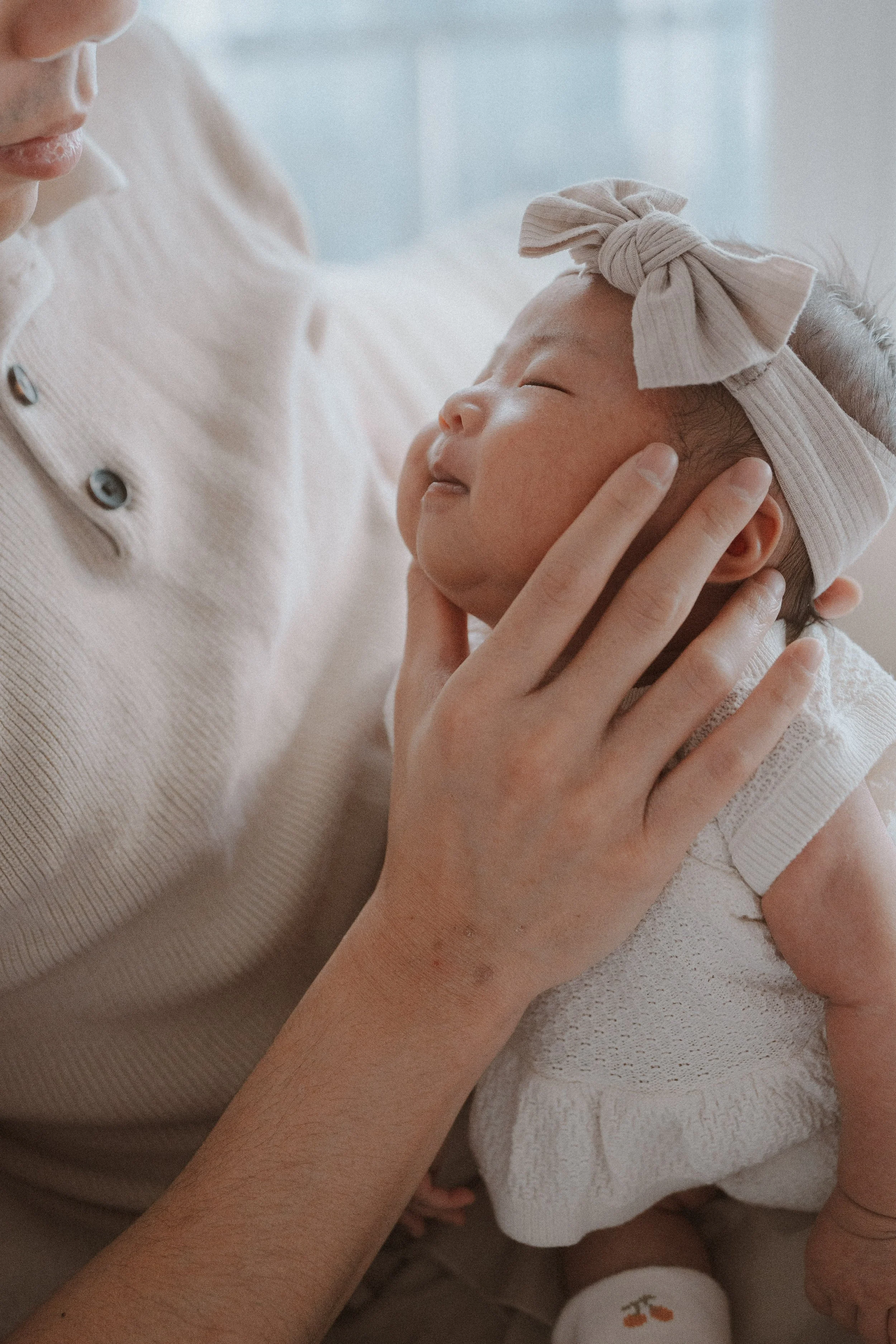 Father Lemon tenderly cradling his newborn baby girls face in his hands while she smiles featuring natural light with soft textures and warm hues in Vancouver.
