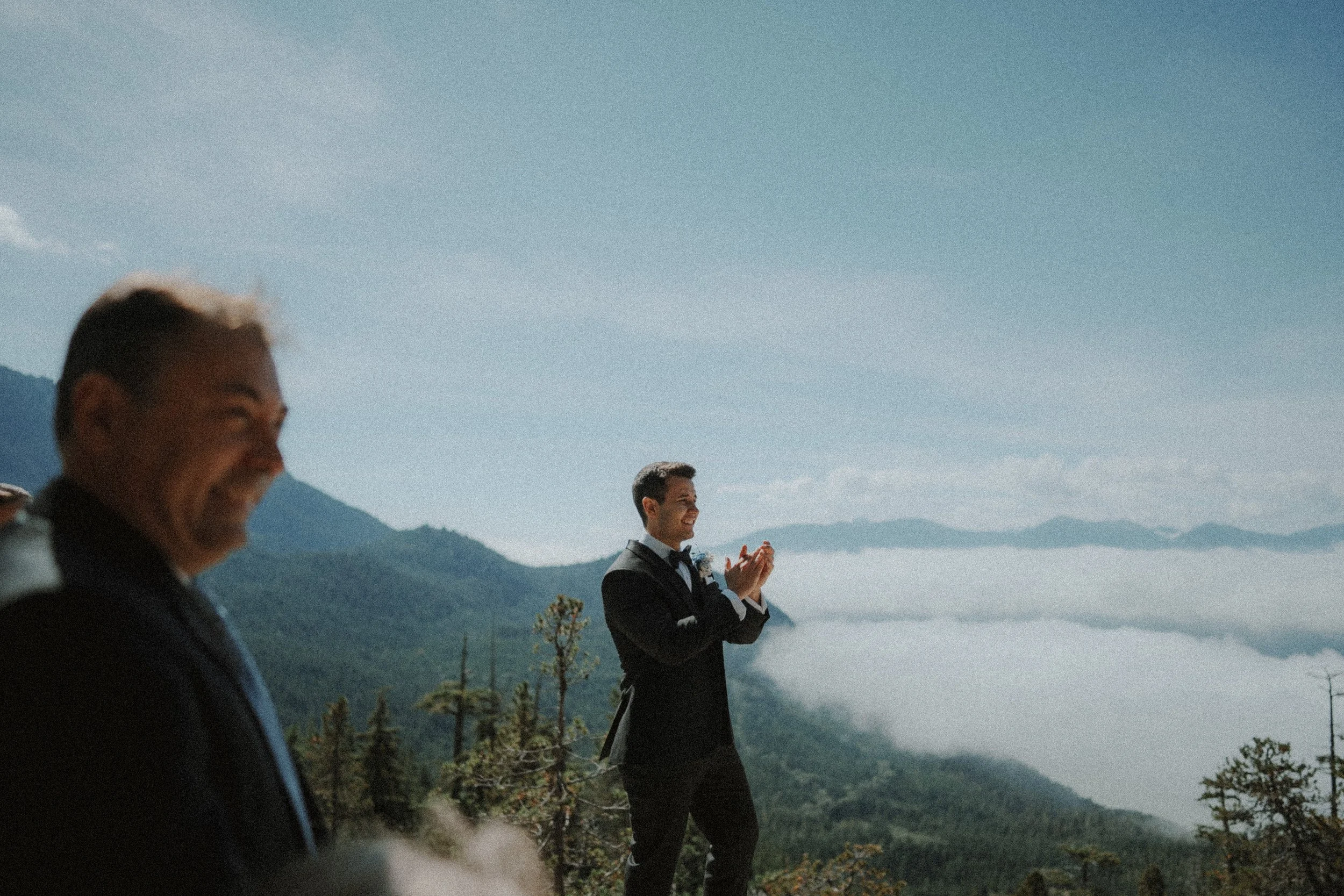 Groom applauding as the wedding ceremony begins above the mountains.