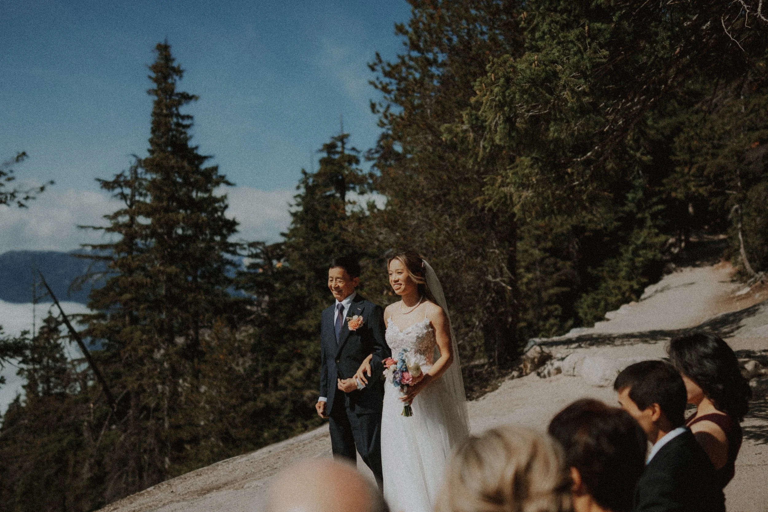 Bride approaching the ceremony arm in arm with an accompanying guest.