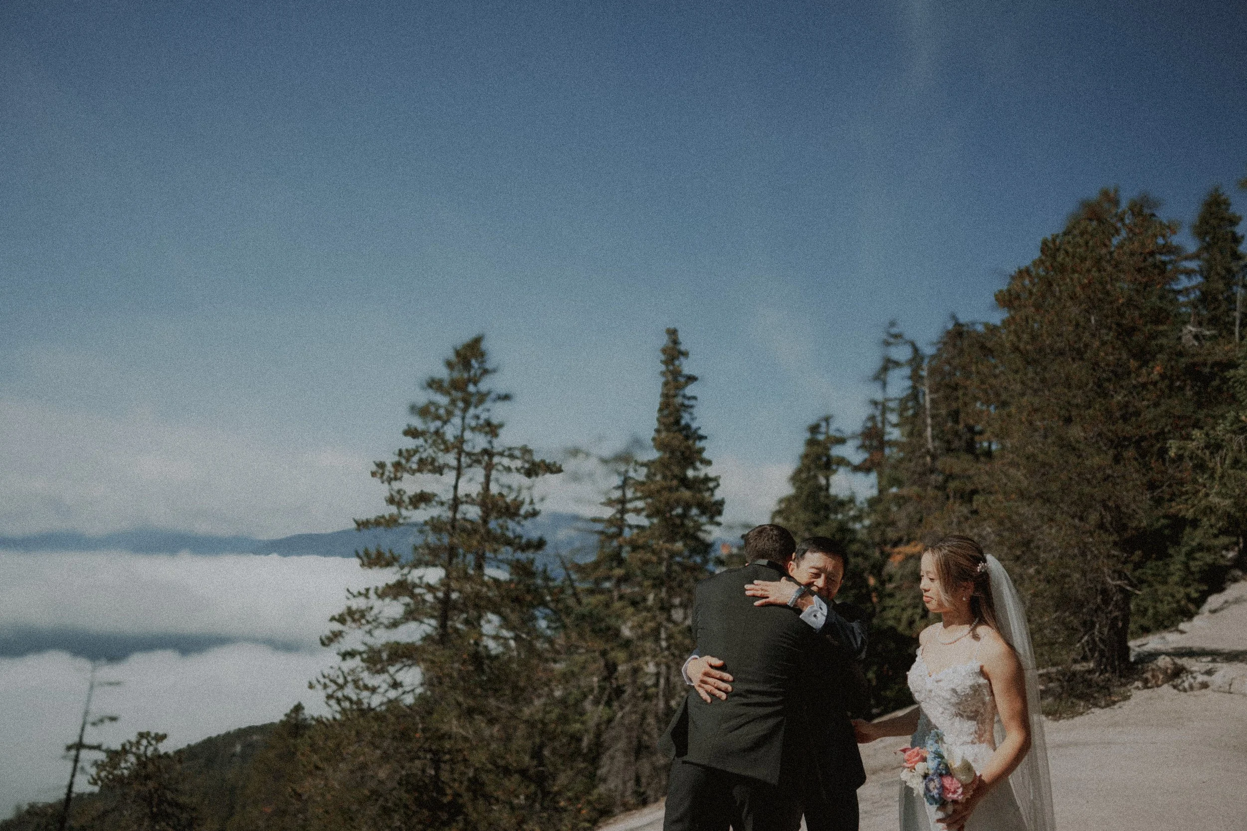 Bride watching as the groom embraces her accompanying guest.