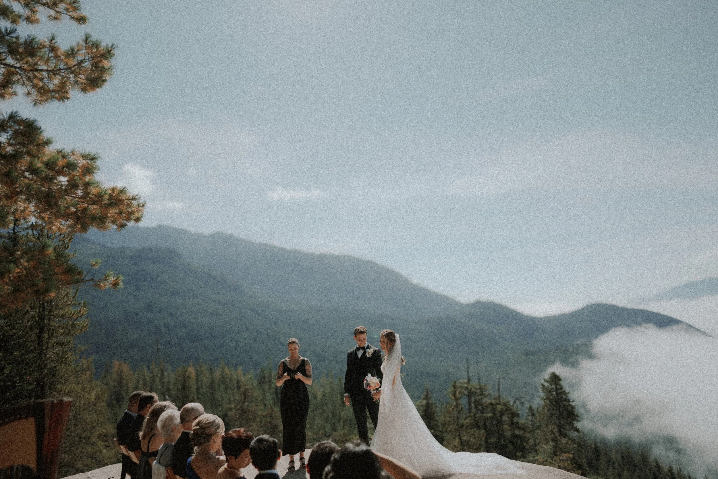 Wedding guests watching the mountain ceremony from wooden chairs.