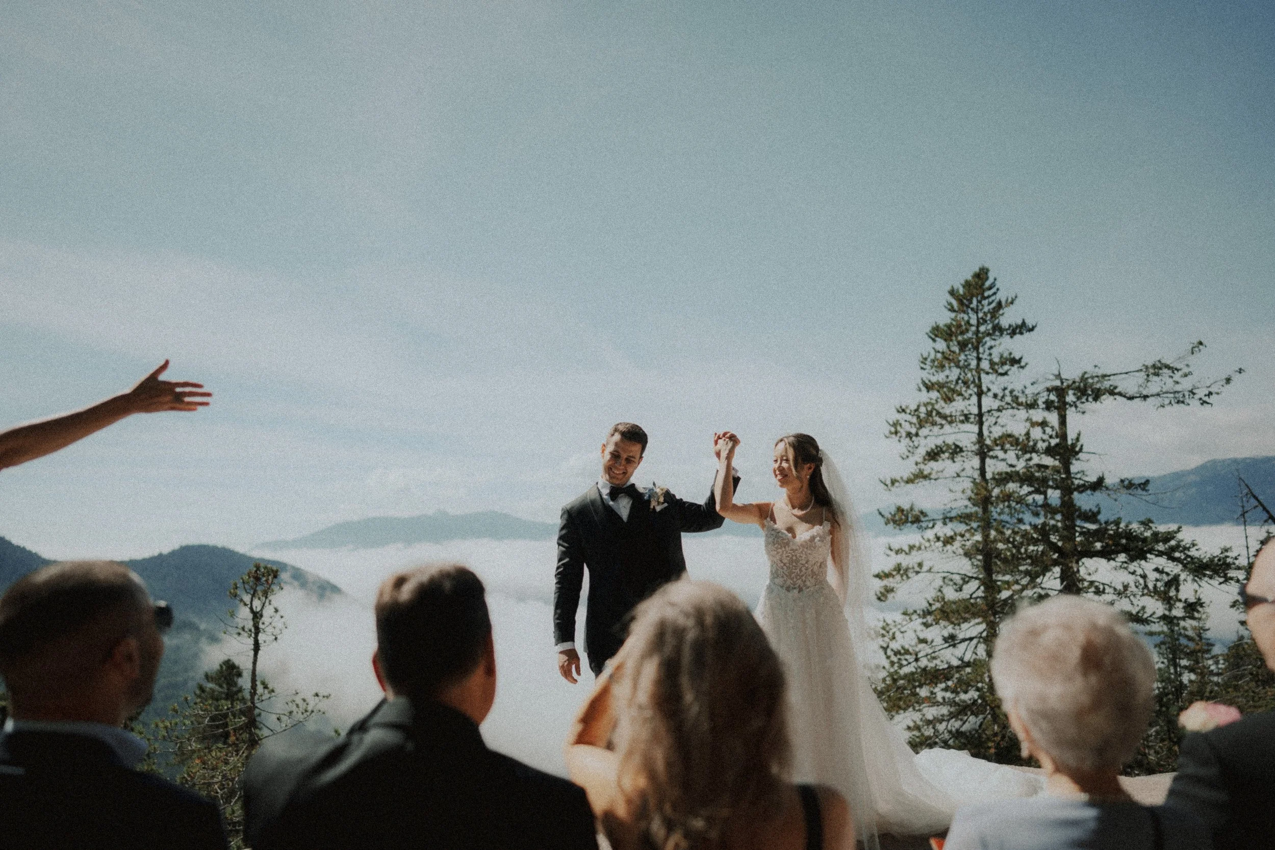 Newlyweds raising their joined hands as guests celebrate.