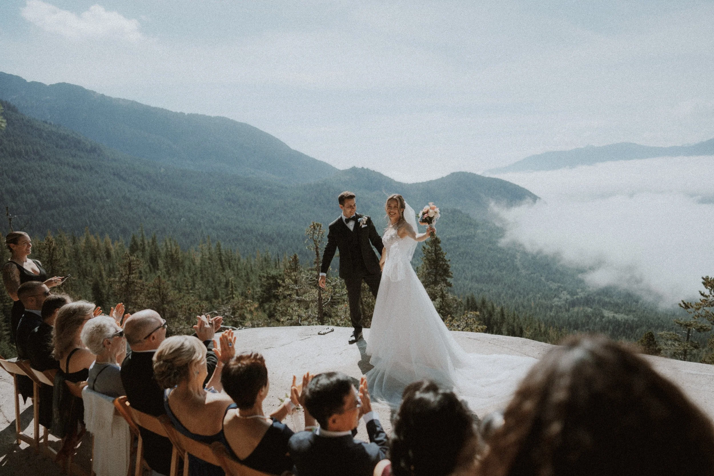 Newlyweds lifting their arms to celebrate with seated wedding guests.