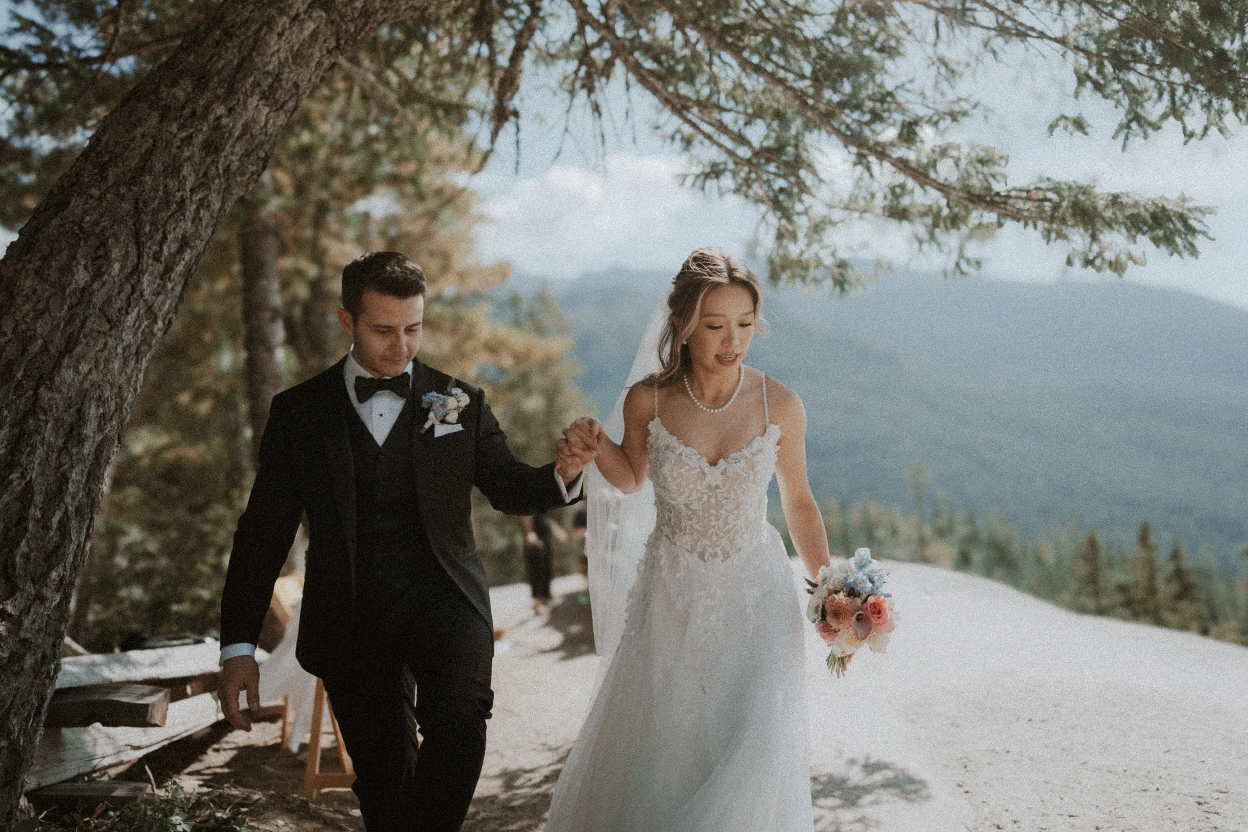 Newlyweds walking beneath sunlit branches after their ceremony.