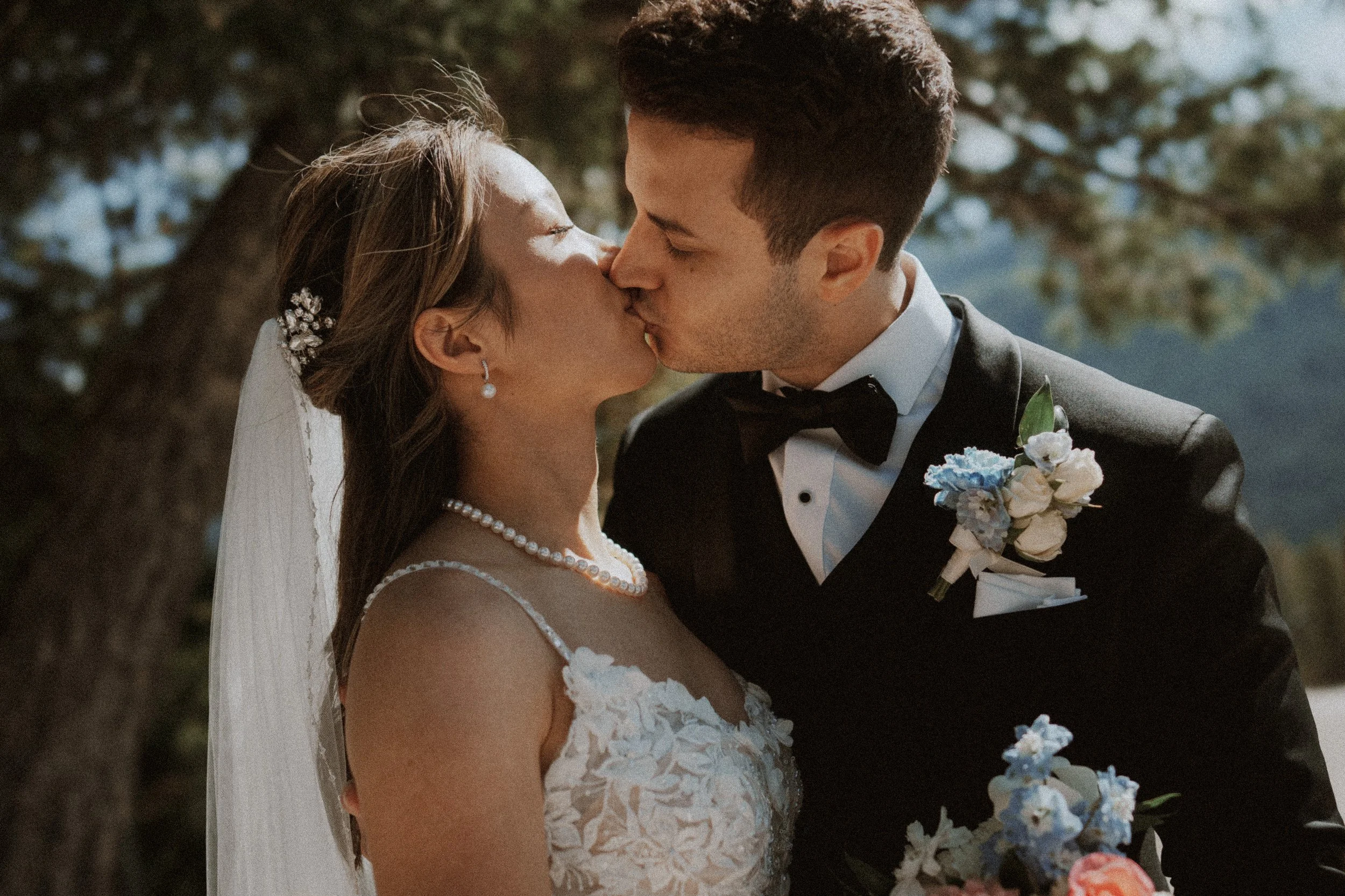 Close-up of the newlyweds kissing in dappled sunlight.