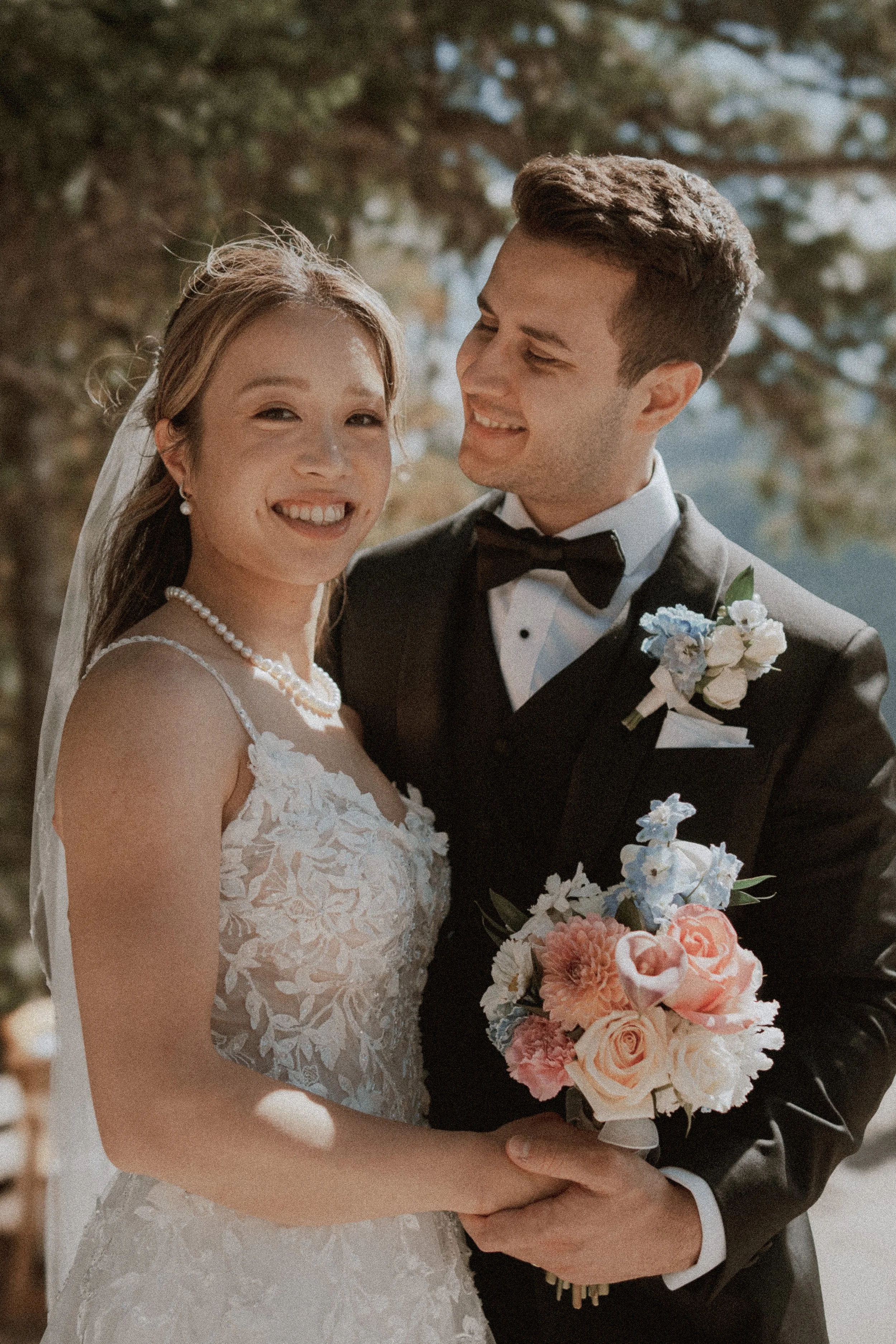 Bride holding a pink bouquet as the groom smiles toward her.