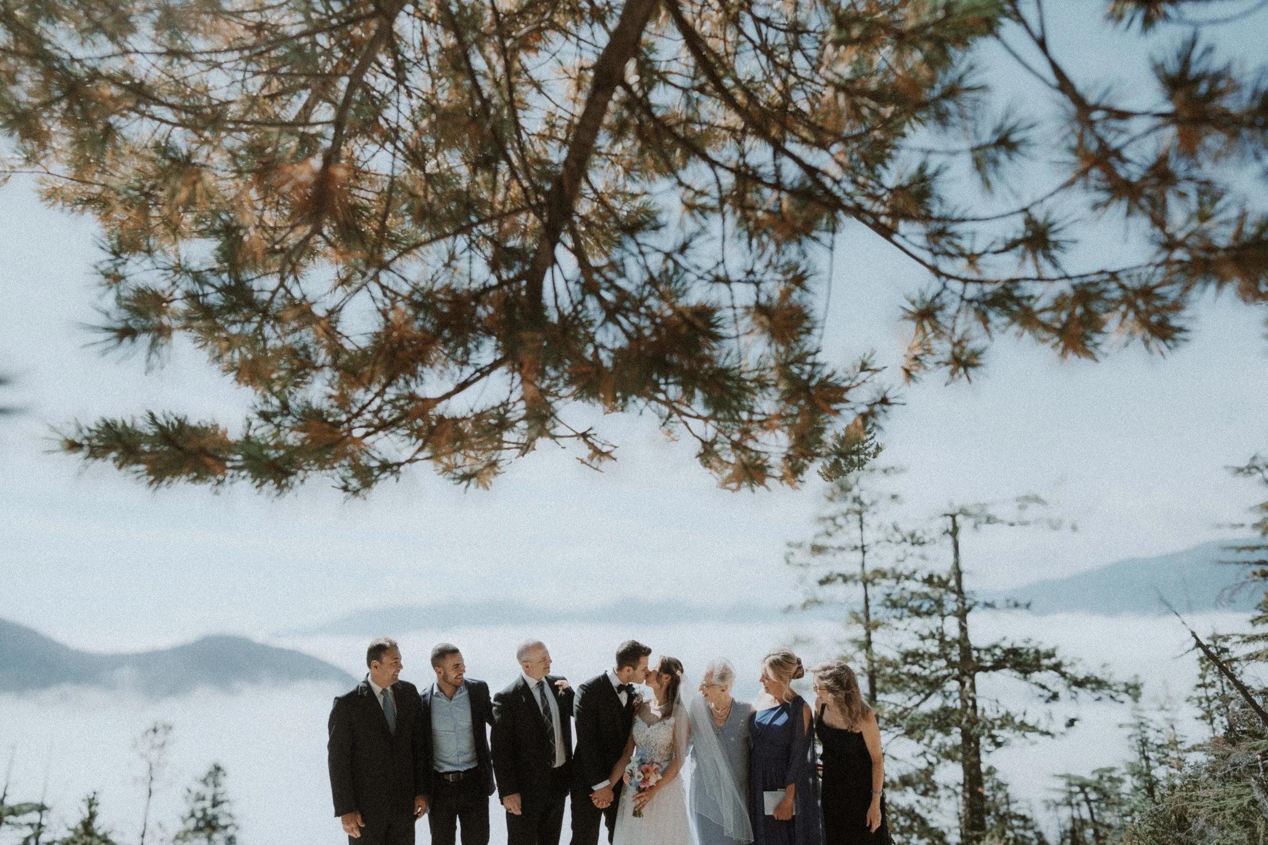Group wedding portrait overlooking clouds and mountain ridges at Sea to Sky Gondola.